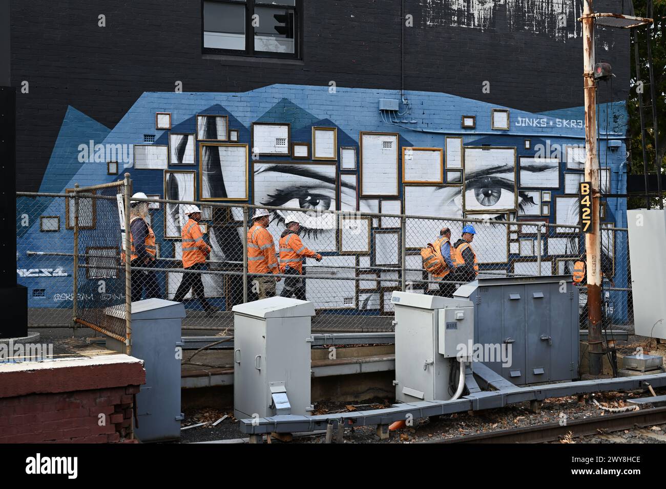 Eine Gruppe von Bahnarbeitern, die orangefarbene Warnwesten und Schutzhelme tragen, geht an einem großen Wandgemälde vorbei, wenn sie den Bahnhof Middle Brighton verlassen Stockfoto