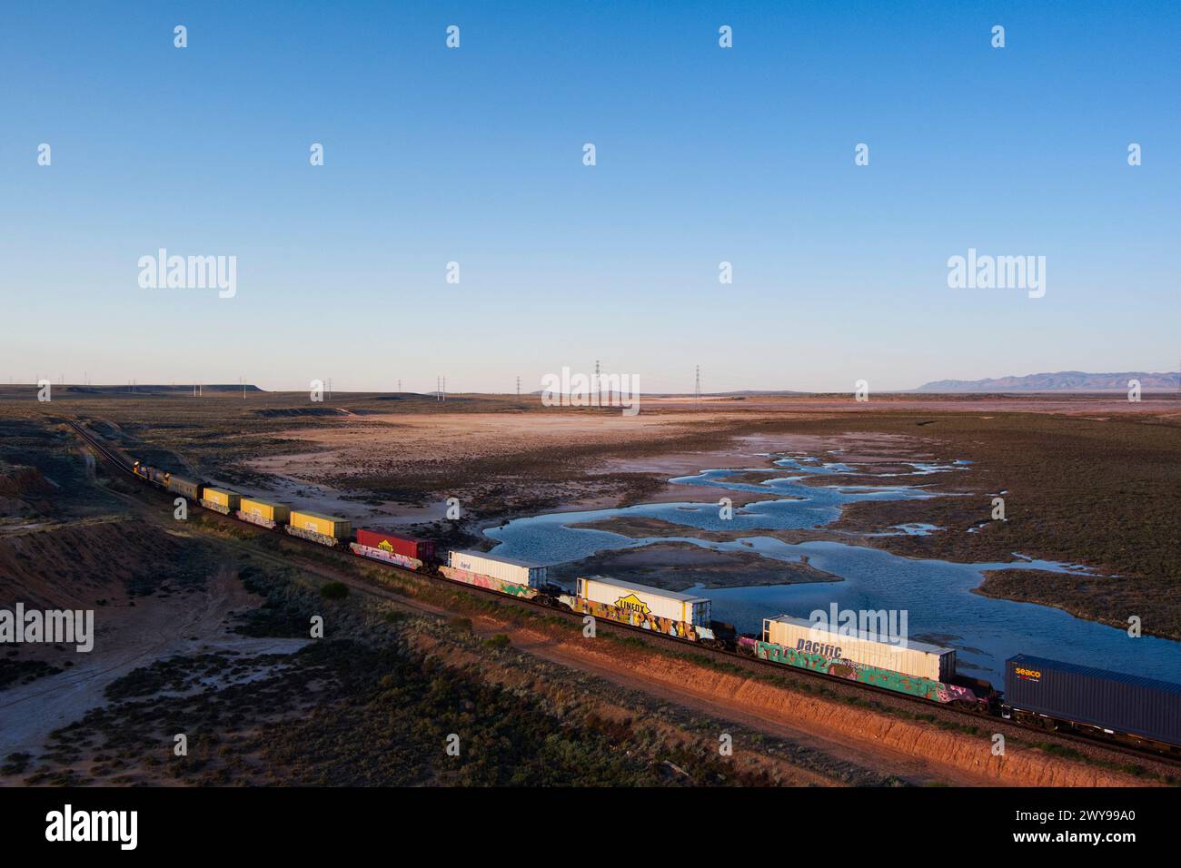 Aus der Vogelperspektive eines intermodalen Container-Güterzugs, der in der Abenddämmerung durch eine riesige Wüstenlandschaft in der Nähe von Port Augusta South Australia fährt Stockfoto