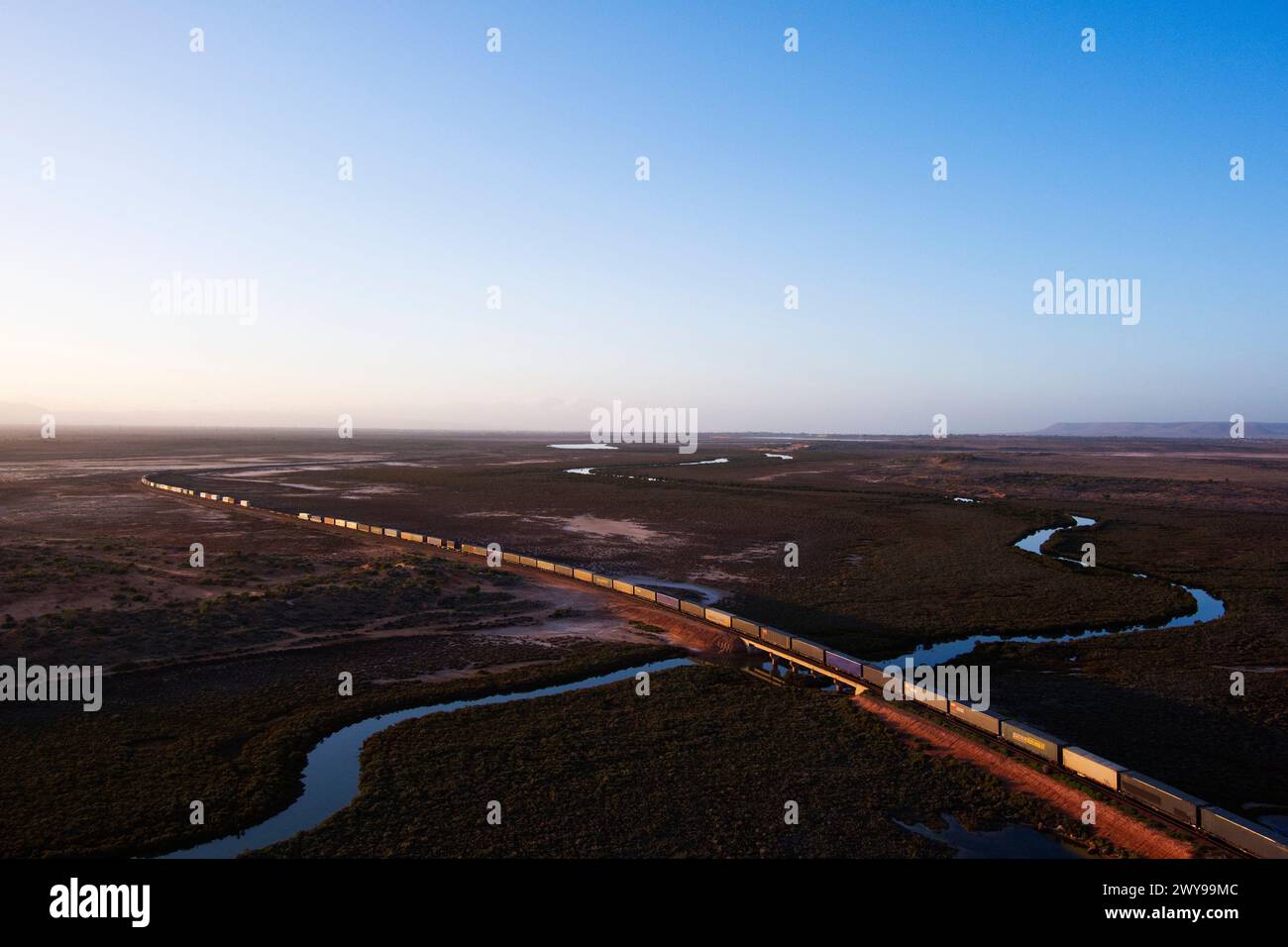 Aus der Vogelperspektive eines intermodalen Container-Güterzugs, der in der Abenddämmerung durch eine riesige Wüstenlandschaft in der Nähe von Port Augusta South Australia fährt Stockfoto