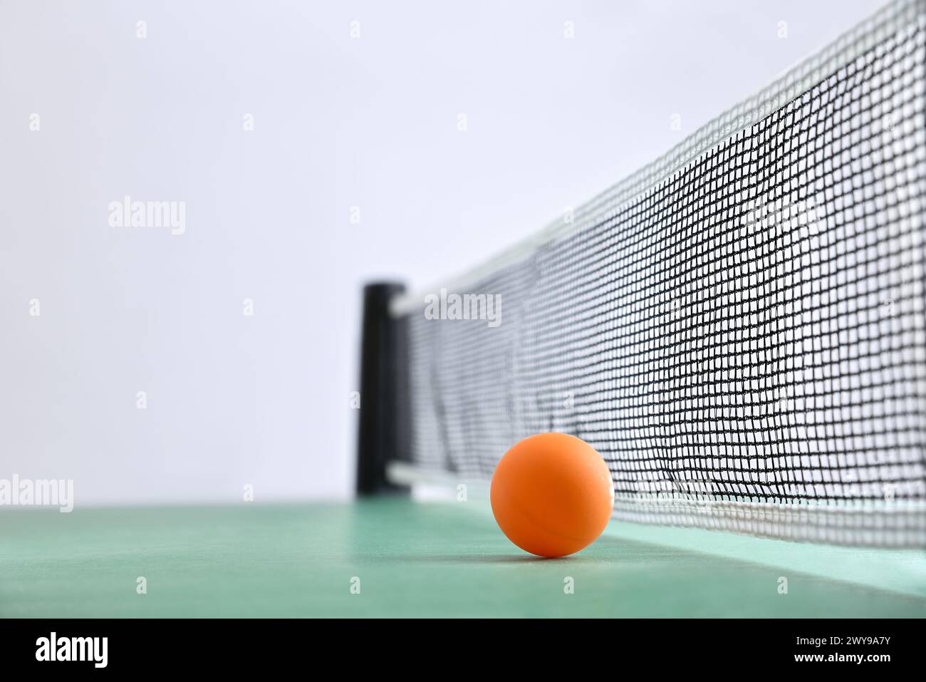 Pingpong-Hintergrund mit orangefarbener Kugel neben dem Netz auf einem grünen Spieltisch und weißem isolierten Hintergrund. Vorderansicht. Stockfoto