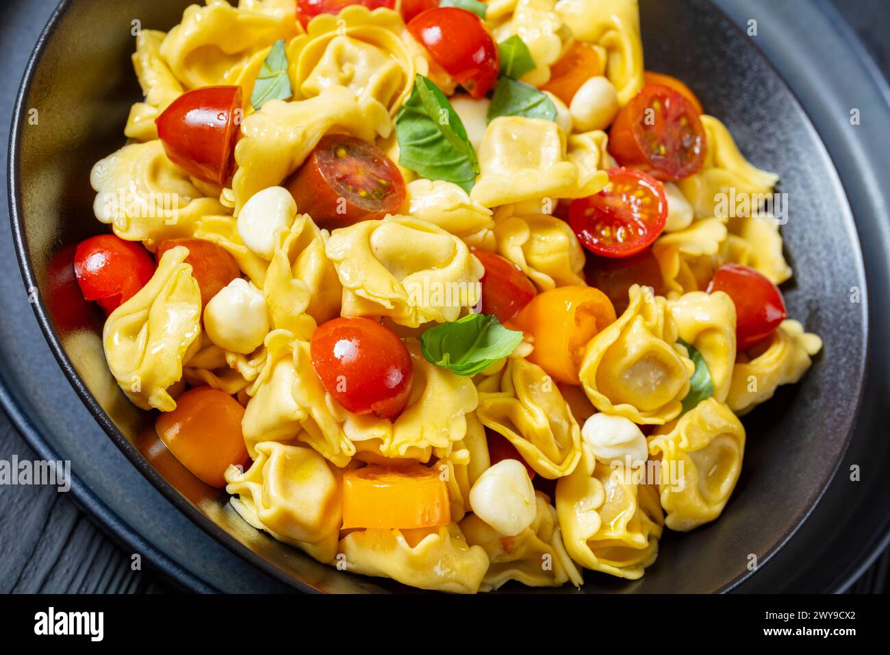 Nahaufnahme von Tortellini-Salat mit Kirschtomaten, Mini-Mozzarella, frischen Basilikumblättern in schwarzer Schüssel Stockfoto