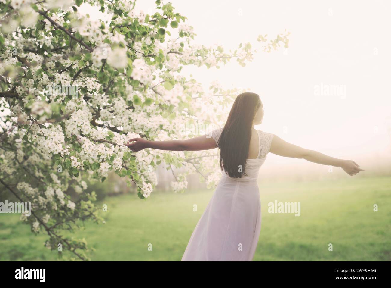 Junge Frau in weiß gekleidet, die mitten in der Frühlingsnatur einen Atem nimmt Stockfoto