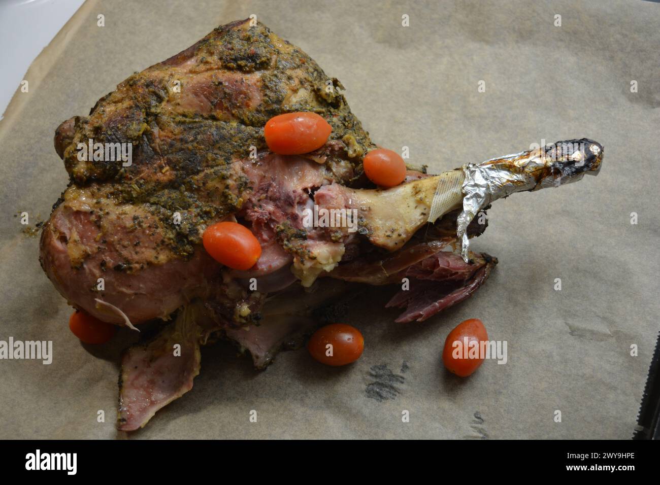 Essen, Kochen köstliches Fleisch, Schafskeule auf dem Knochen mariniert und im Ofen gebacken. Ein großes Stück Lammfleisch auf braunem Pergamentpapier/ Stockfoto