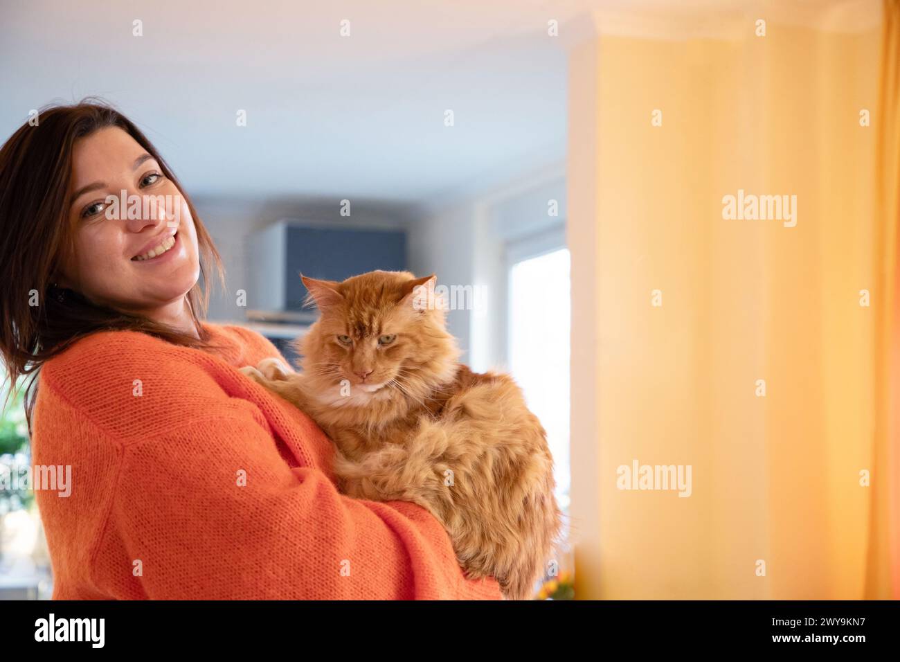 Eine junge Frau, die einen warmen Pullover trägt, ruht sich zu Hause bei der Katze aus Stockfoto