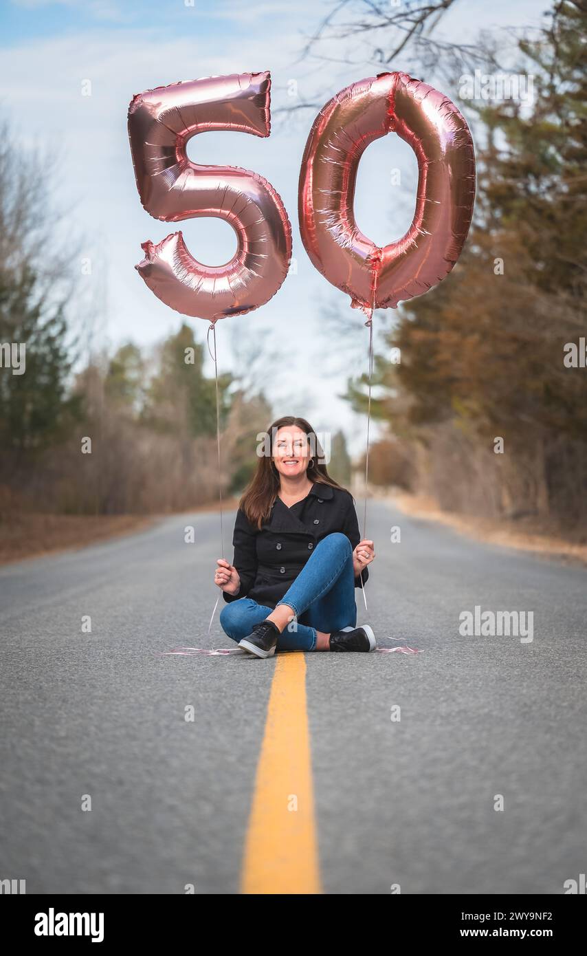 Porträt einer Frau, die auf der Straße sitzt und 50 Ballons hält. Stockfoto