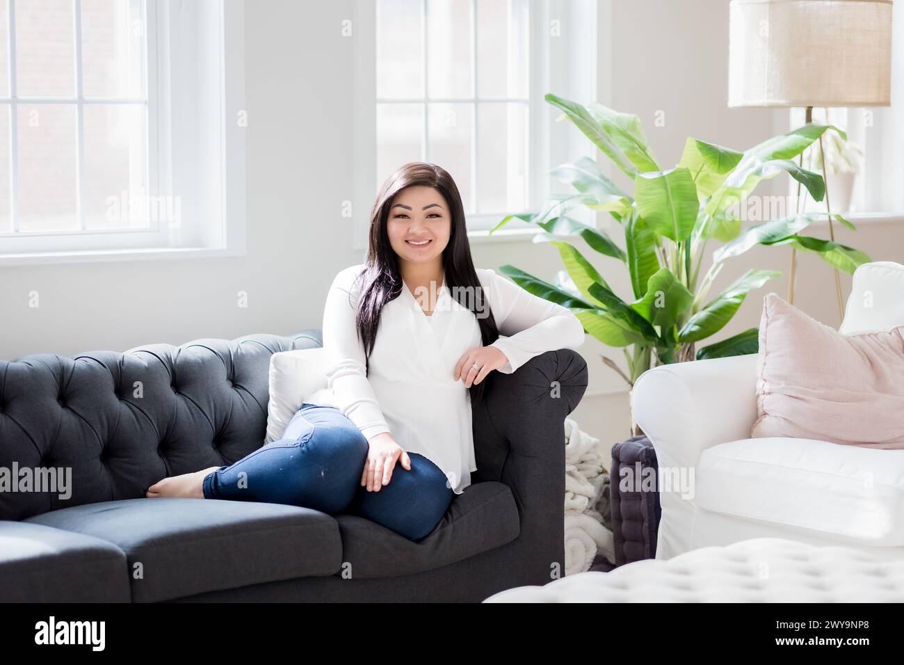 Junge asiatische Frau lächelt und sitzt in einem hellen, luftigen Sofa Stockfoto