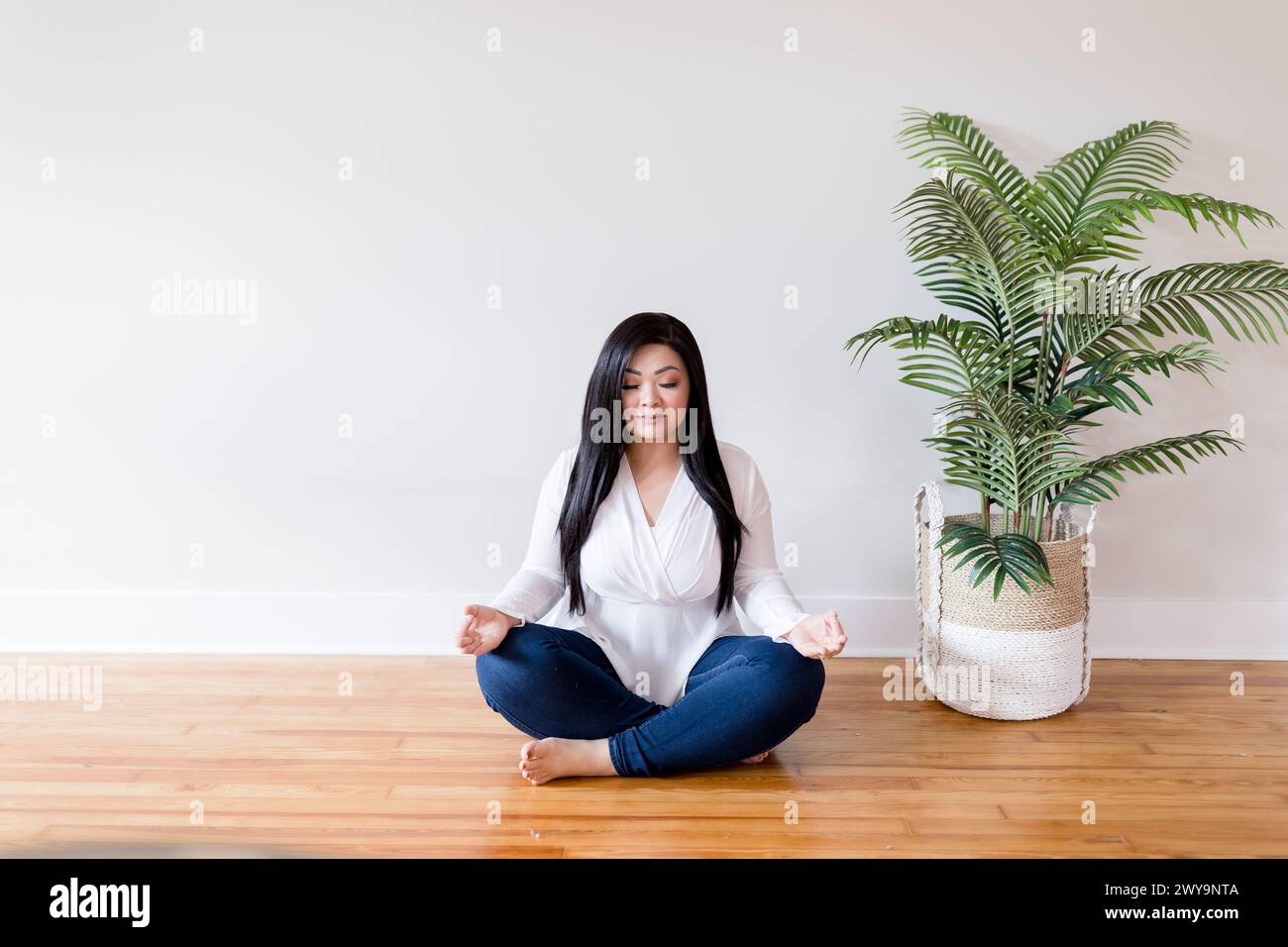 Asiatische Frau, die auf Holzboden sitzt, überkreuzte Beine beim Meditieren Stockfoto