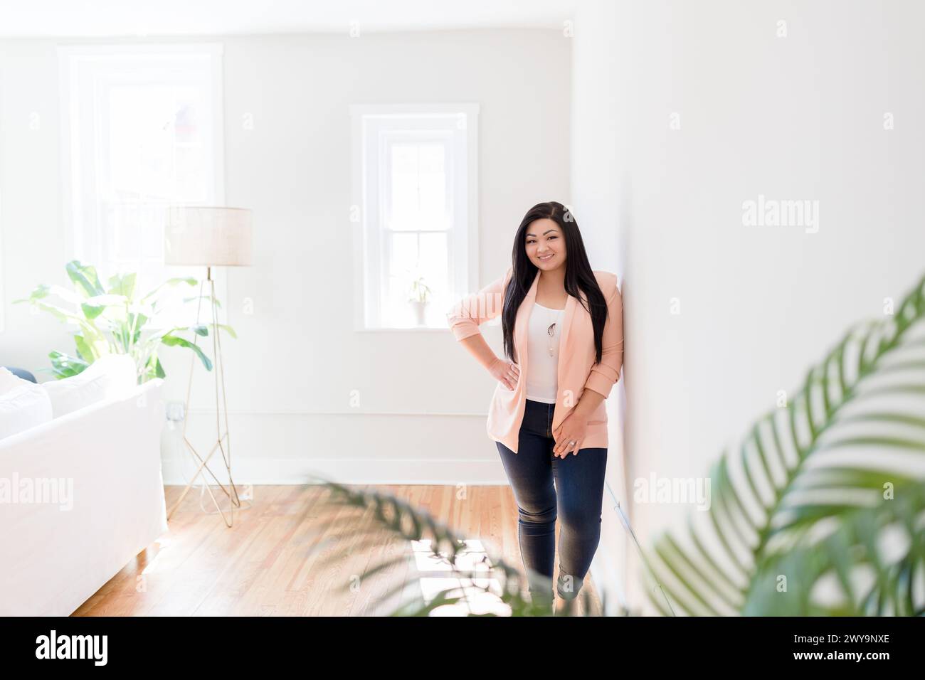 Lächelnde asiatische Frau, die in einem hellen, minimalistischen Haus mit Plan steht Stockfoto