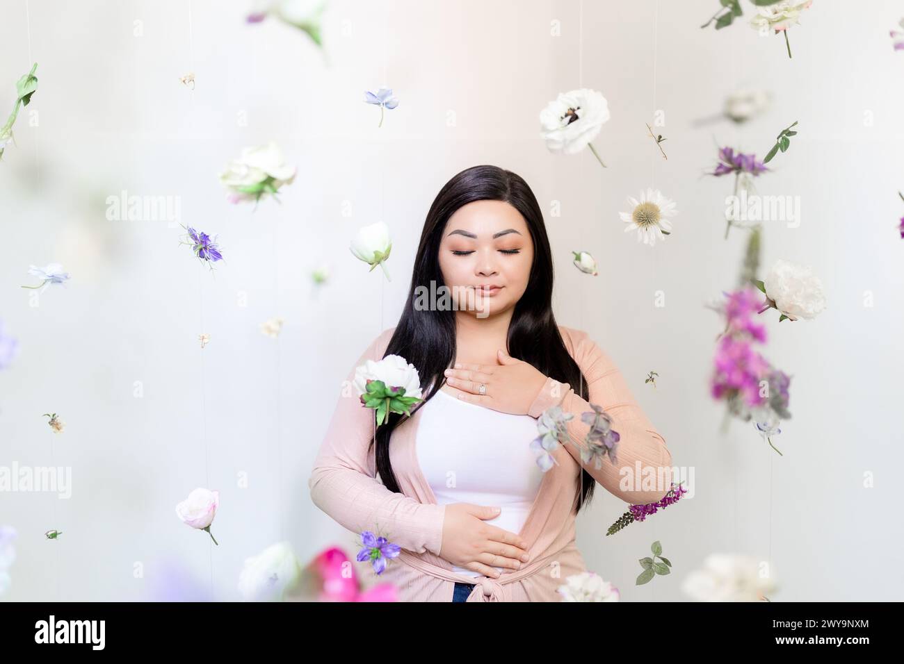 Zen asiatische Frau meditiert zwischen hängenden lila und rosa Blüten Stockfoto