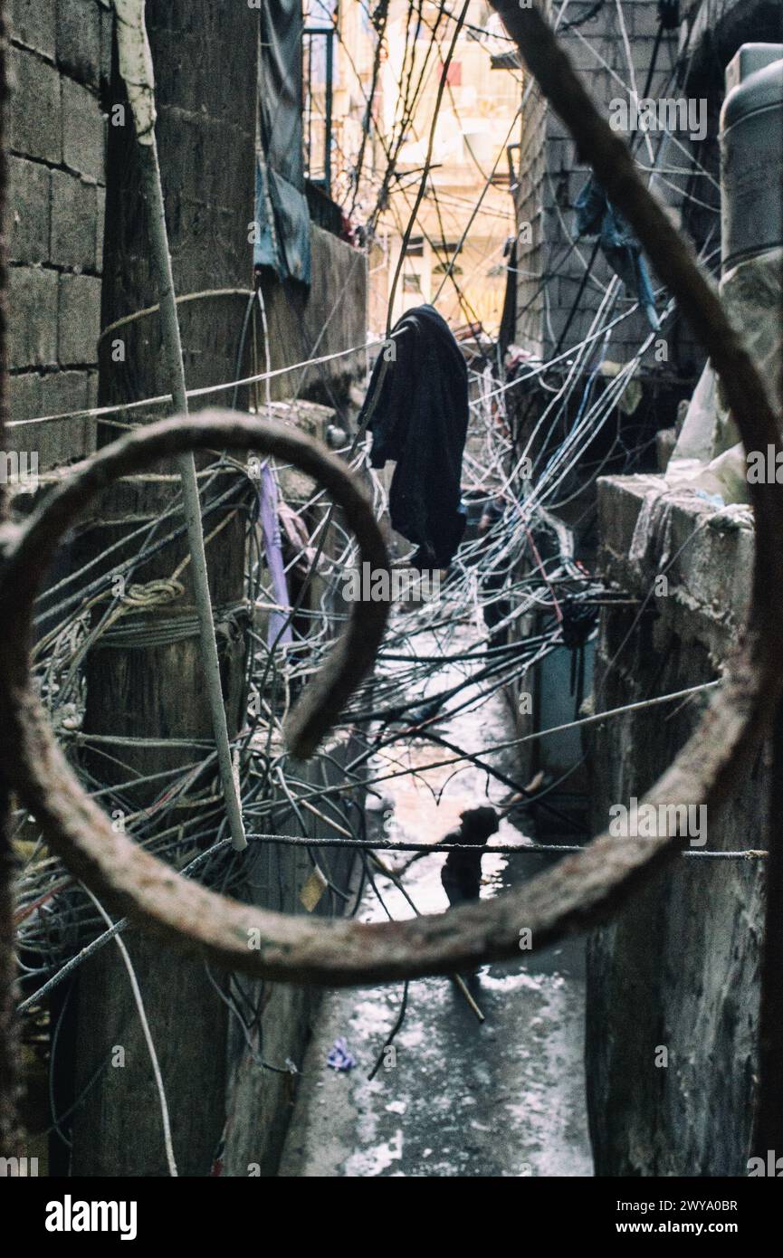 Chaotischer Blick auf die elektrischen Leitungen mit einer Frau, die auf der Straße des Flüchtlingslagers Sabra-Shatila im Libanon läuft Stockfoto