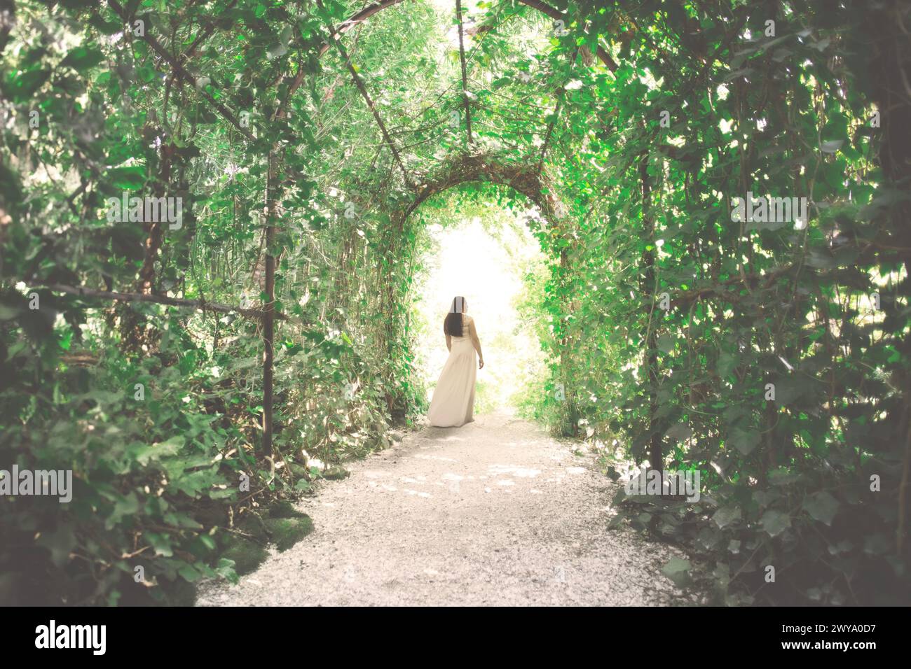Elegante junge Frau geht glücklich zum Ausgang eines Tunnels, der von üppigen Pflanzen gebildet wird Stockfoto