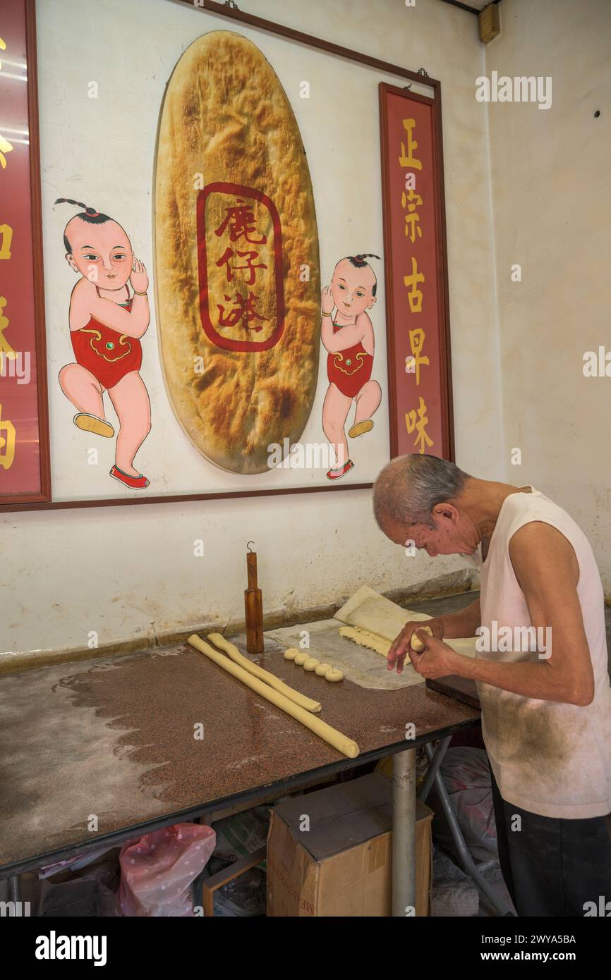 Ein älterer Mann, der Brot in einem kleinen Laden mit chinesischem Schild macht Stockfoto