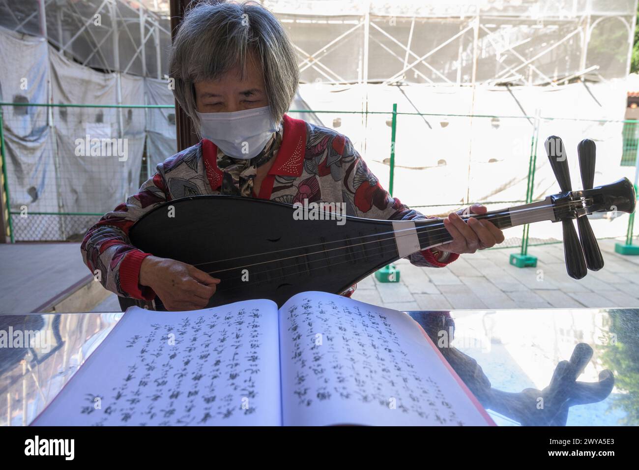 Eine ältere Frau spielt ein traditionelles chinesisches Streichinstrument mit einer Maske Stockfoto