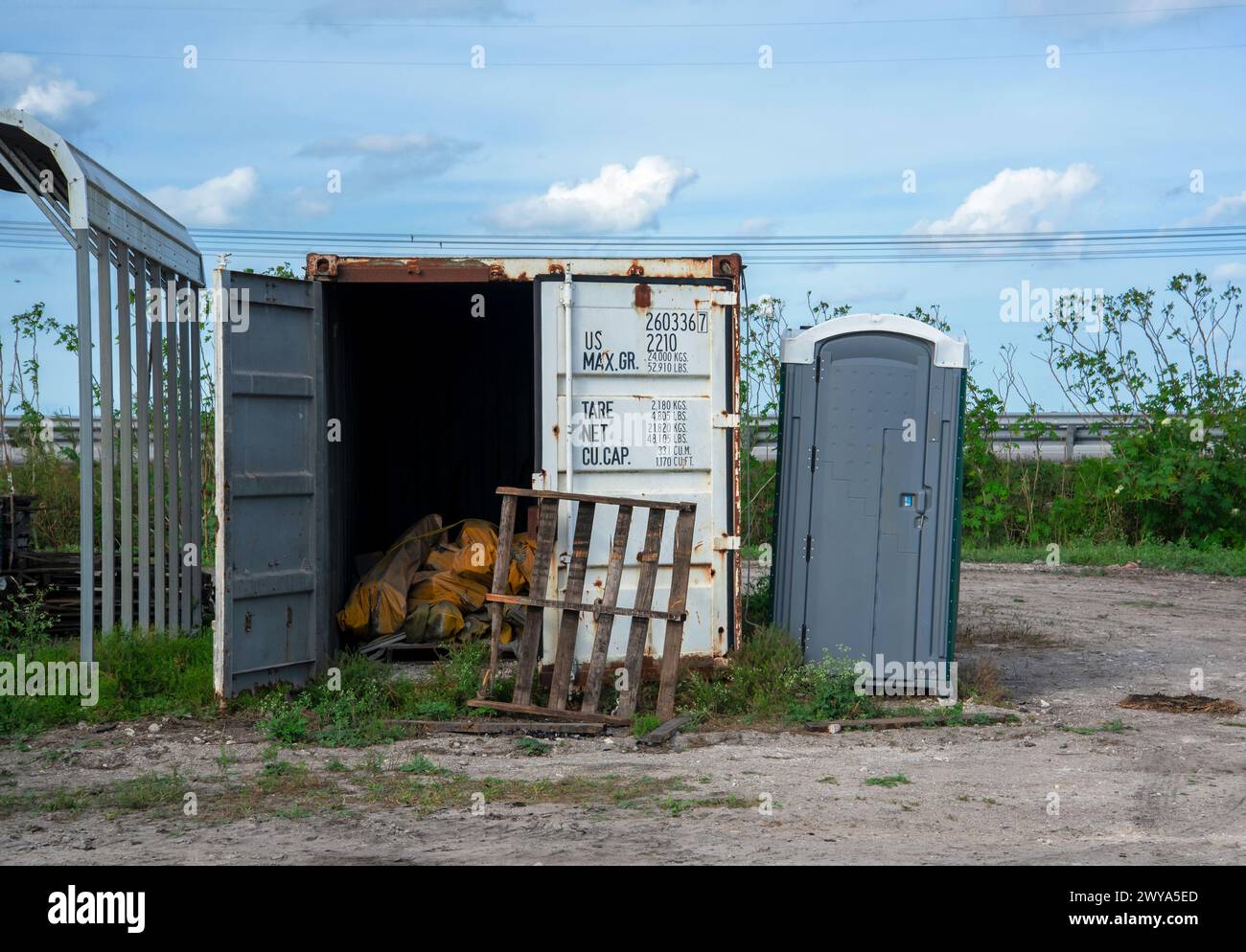 Ein offener Versandcontainer und ein Portapotty, eine alte Holzpalette, die sich gegen die geschlossene Tür lehnte. Stockfoto