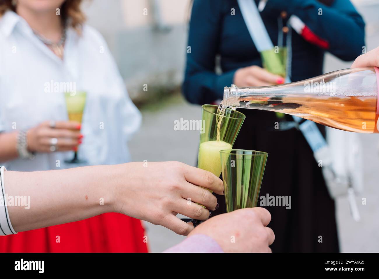 Eine Frau gießt Wein in zwei grüne Gläser. Die Gläser sind mit Wein gefüllt und die Frau hält sie an den Mund. Die Szene spielt in A Stockfoto