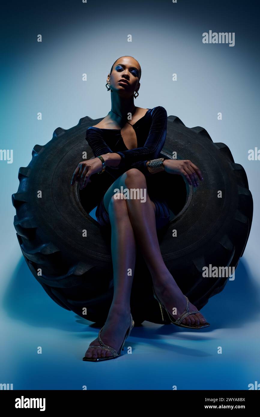 Eine junge afroamerikanische Frau sitzt selbstbewusst auf einem kolossalen Reifen in einem kreativen Studio-Setting. Stockfoto