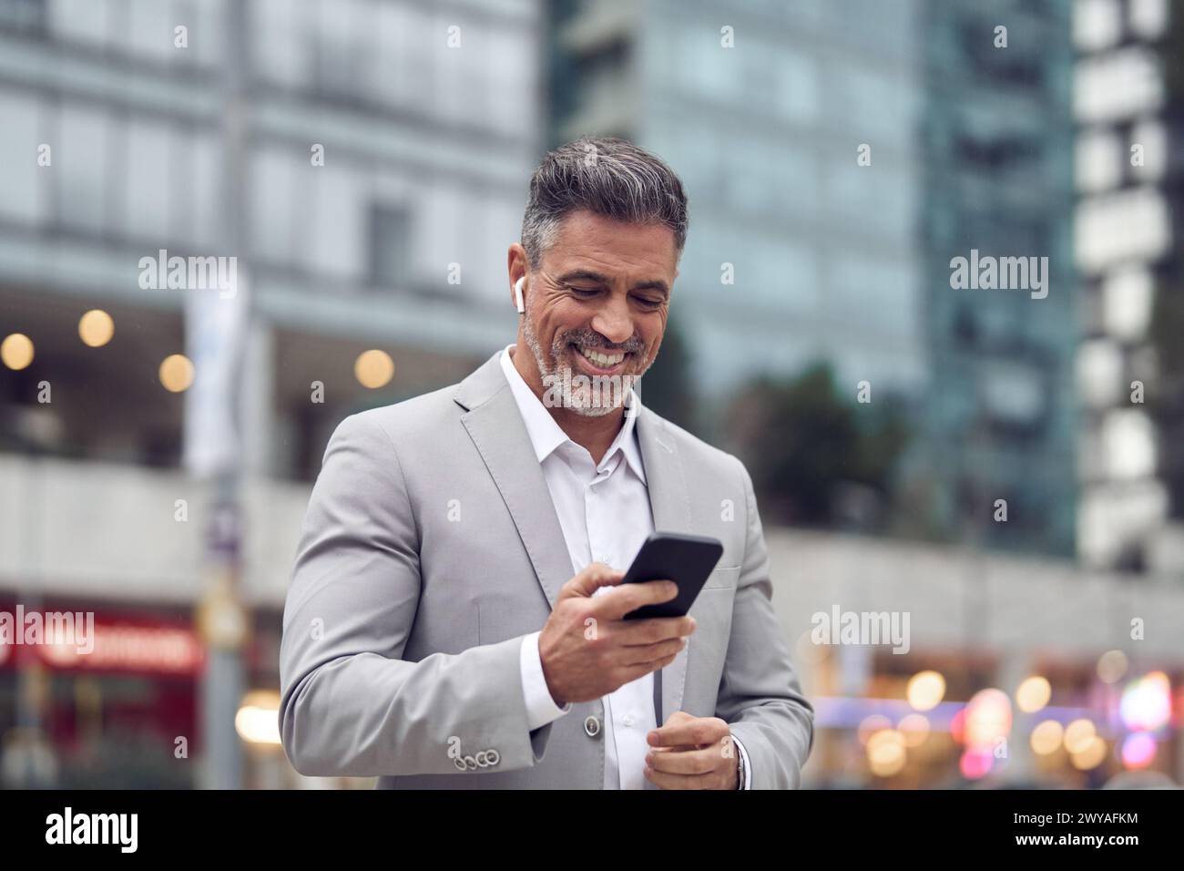 Glücklicher Geschäftsmann mittleren Alters, der Ohrstöpsel trägt, indem er auf der Straße der Stadt läuft. Stockfoto