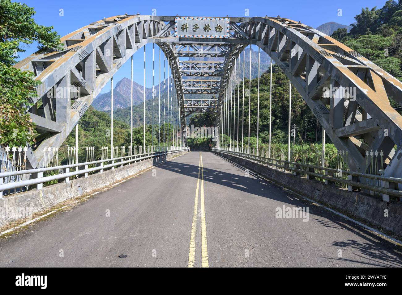 Eine symmetrische Metallbrücke über eine gerade Straße mit deutlichen Markierungen, die in Richtung entfernter Berge in der Meishan Township führt Stockfoto