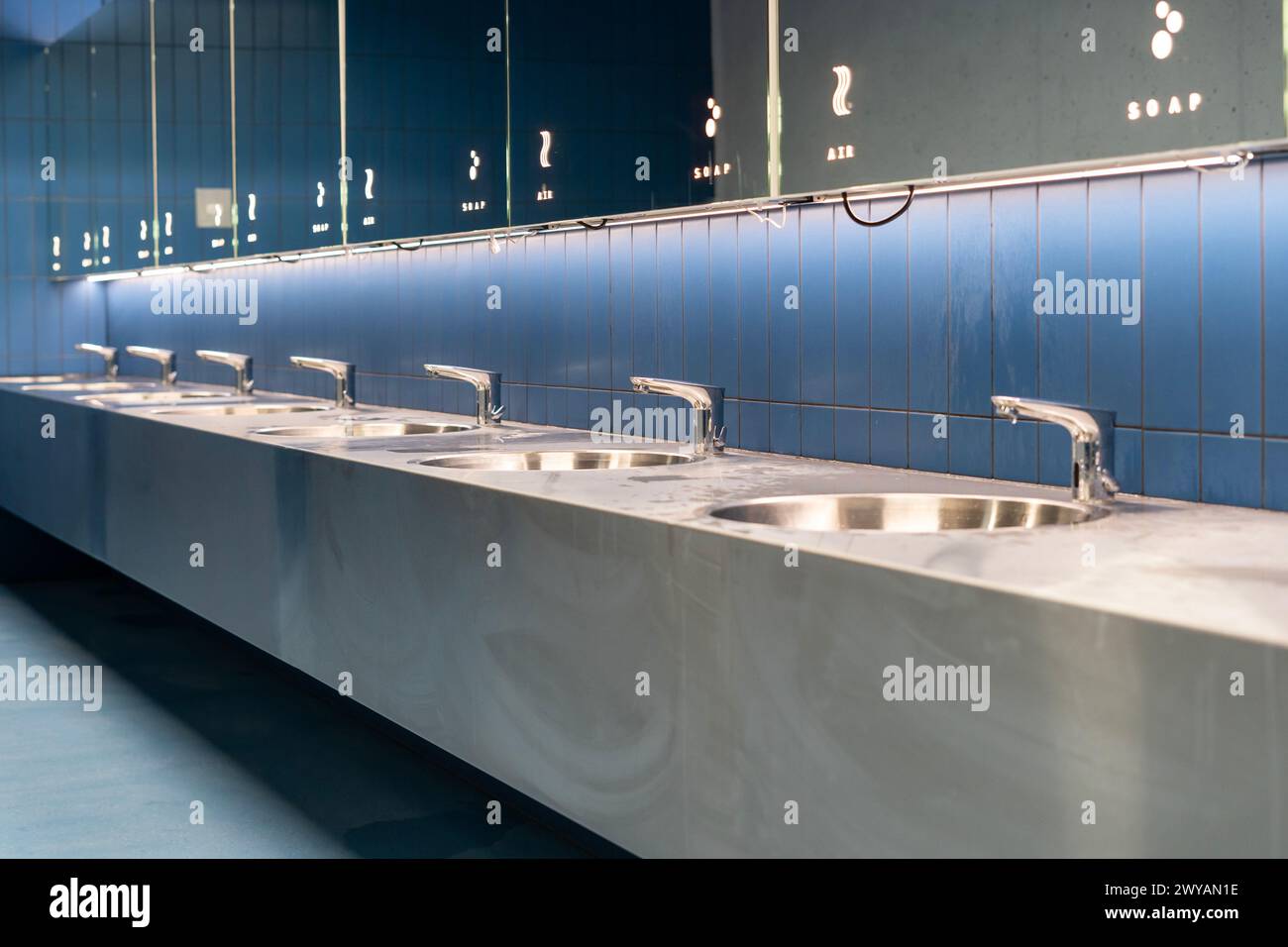 Eine Reihe Waschbecken mit Spiegeln in einer blau gefliesten öffentlichen Toilette Stockfoto