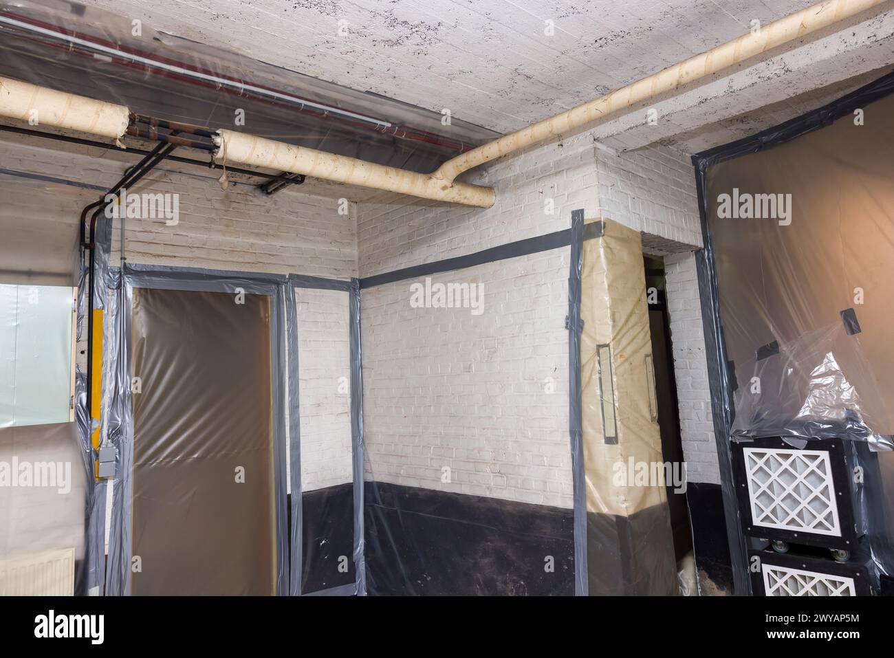 Die Asbestentfernung funktioniert bei der Isolierung von Heizungsrohren in einem Keller, bei dem alle Wände mit Kunststoff bedeckt sind, und die Absaugung von gefilterter Luft dient, um VE zu entfernen Stockfoto