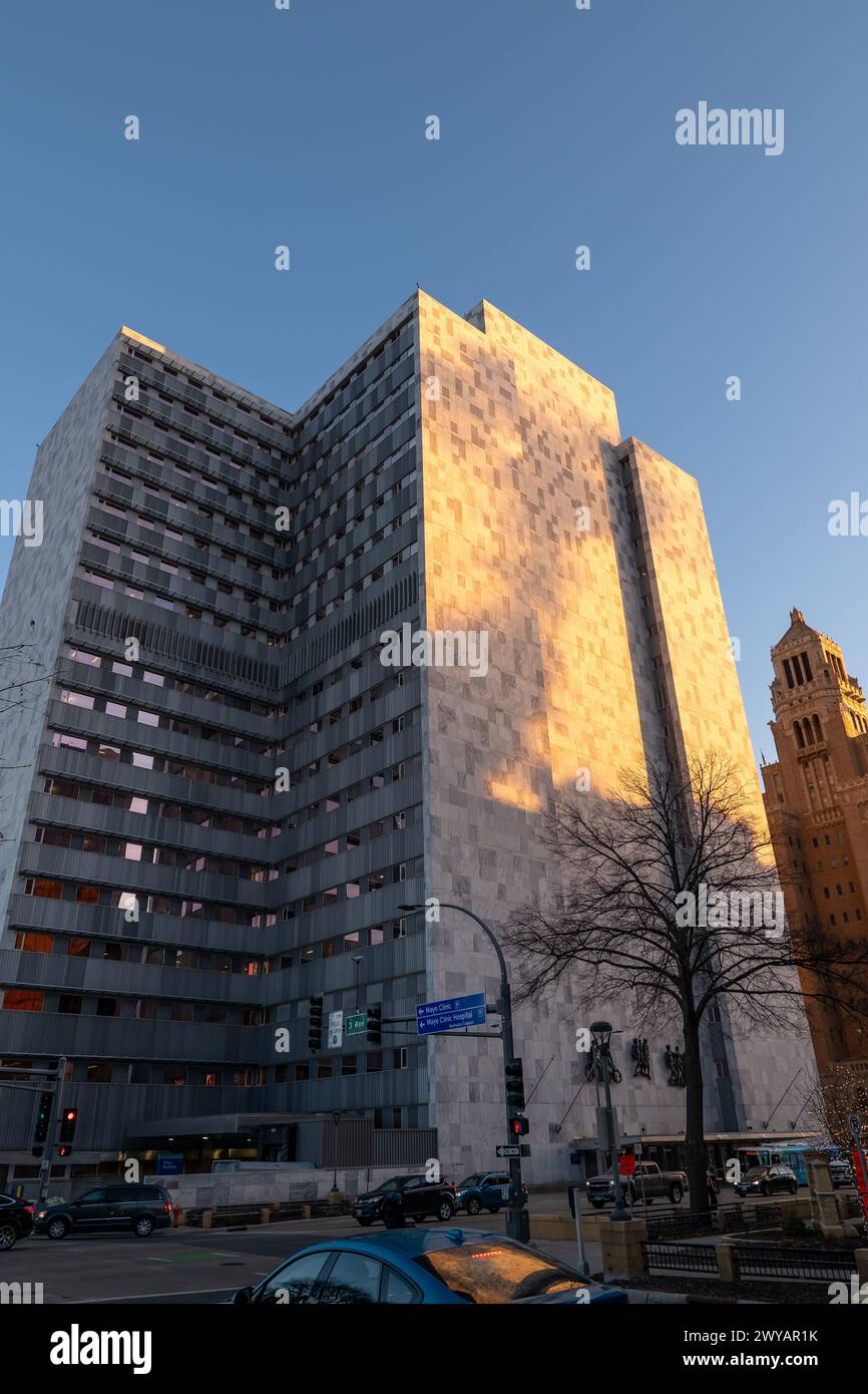 ROCHESTER, MN – 14. Dezember 2023: Sonnenschein am frühen Morgen auf den oberen Etagen des Mayo Building in Minnesota, während der Verkehr auf den Straßen fließt. Stockfoto