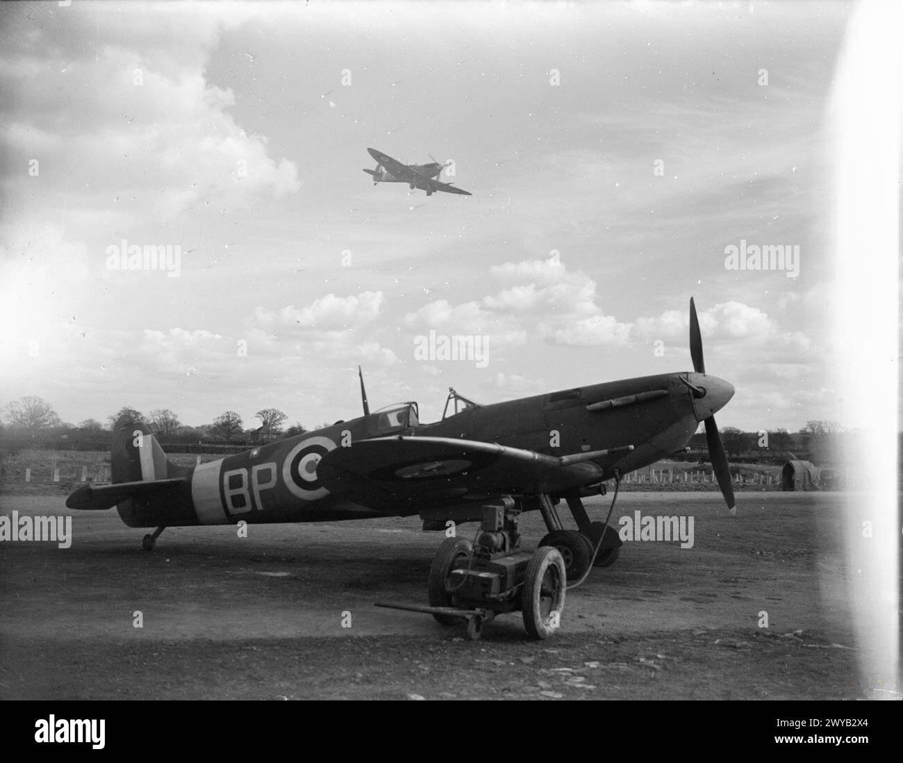 KÖNIGLICHE LUFTWAFFE, 1939-1945. - Supermarine Spitfire Mark VB von der No 457 Squadron RAAF kehrt nach Redhill, Surrey, zurück, nachdem sie Nordfrankreich überflogen hatte, während ein weiteres Squadron-Flugzeug an seinem Ausbreitungspunkt steht und bereit in einen Trolley-Akkumulator gesteckt wurde. Royal Australian Air Force, 457 Squadron Stockfoto