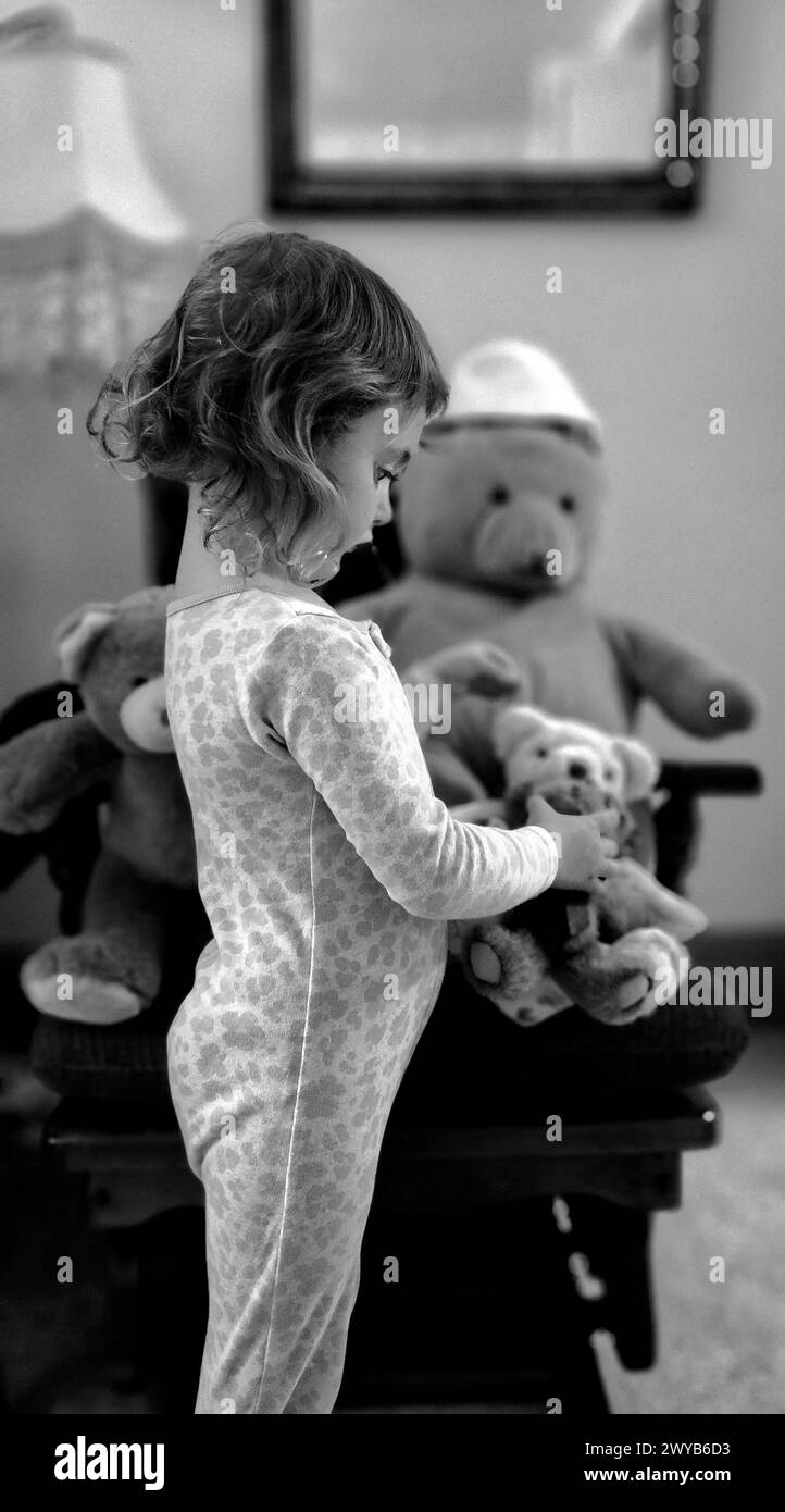 Schwarz-weiß-Foto eines kleinen Mädchens, das einen Teddybären ansieht, den sie hält Stockfoto