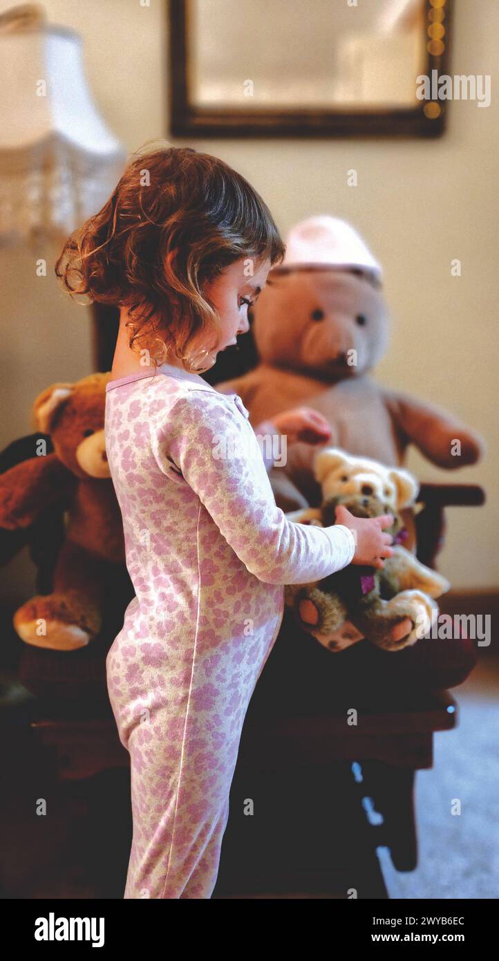 Ein kleines Mädchen, das einen Teddybären ansieht, den sie hält Stockfoto