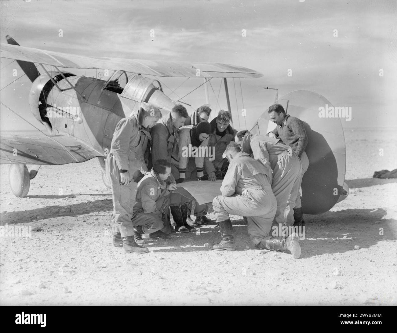 ROYAL AIR FORCE OPERATIONEN IM NAHEN OSTEN UND NORDAFRIKA, 1939-1943. - Piloten der 3. Geschwader RAAF studieren eine Karte auf dem Heckflugzeug eines ihrer Gloster-Gladiatoren auf ihrem Landeplatz bei Sollum, Ägypten, bevor sie während der letzten Phase der Operation KOMPASS über Bardia operieren. Von links nach rechts: Fliegende Offiziere J R Perrin, J MCD Davidson (Squatting), W S Arthur und P St G Turnbull, Flight Lieutenants G H Steege und A C Rawlinson, Flying Officer V East, (unbekannt), Squadron Leader I D McLachlan (Commanding Officer) und Flying Officer A H Boyd. Royal Australian Air Force, 3 Squadro Stockfoto