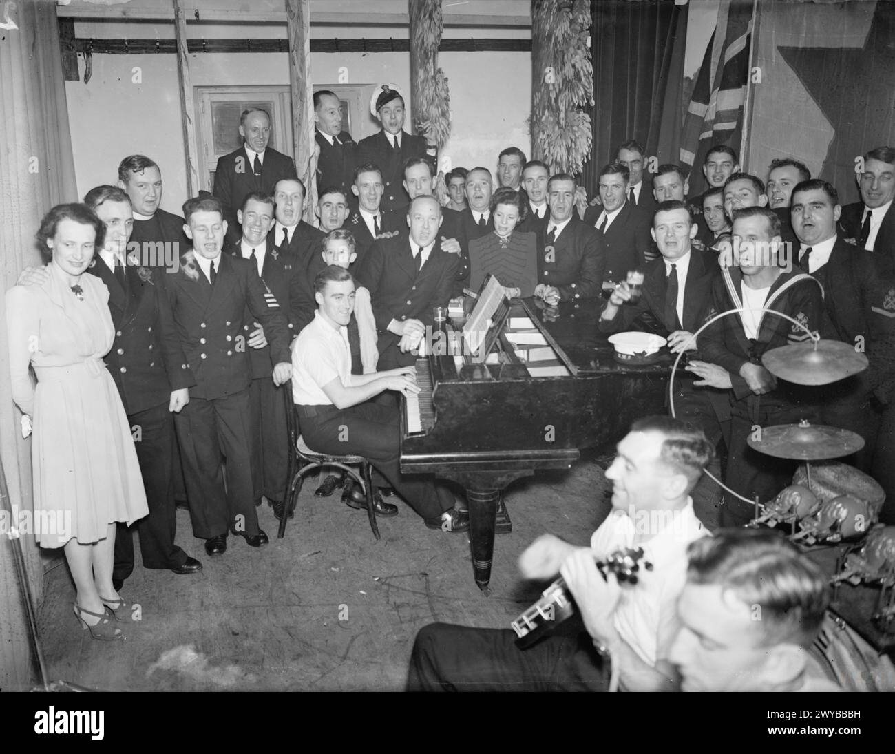 BRITISCHE SEEMANNSFEIER IM NAHEN OSTEN. 25. DEZEMBER 1941, FLEET CLUB, ALEXANDRIA. - Ein Gesangslied am Klavier. Reverend A Spender, MA, Chaplain, RN, (3. Von links) schließt sich einigen der Männer an, die ein paar Lieder am Klavier spielen. , Stockfoto