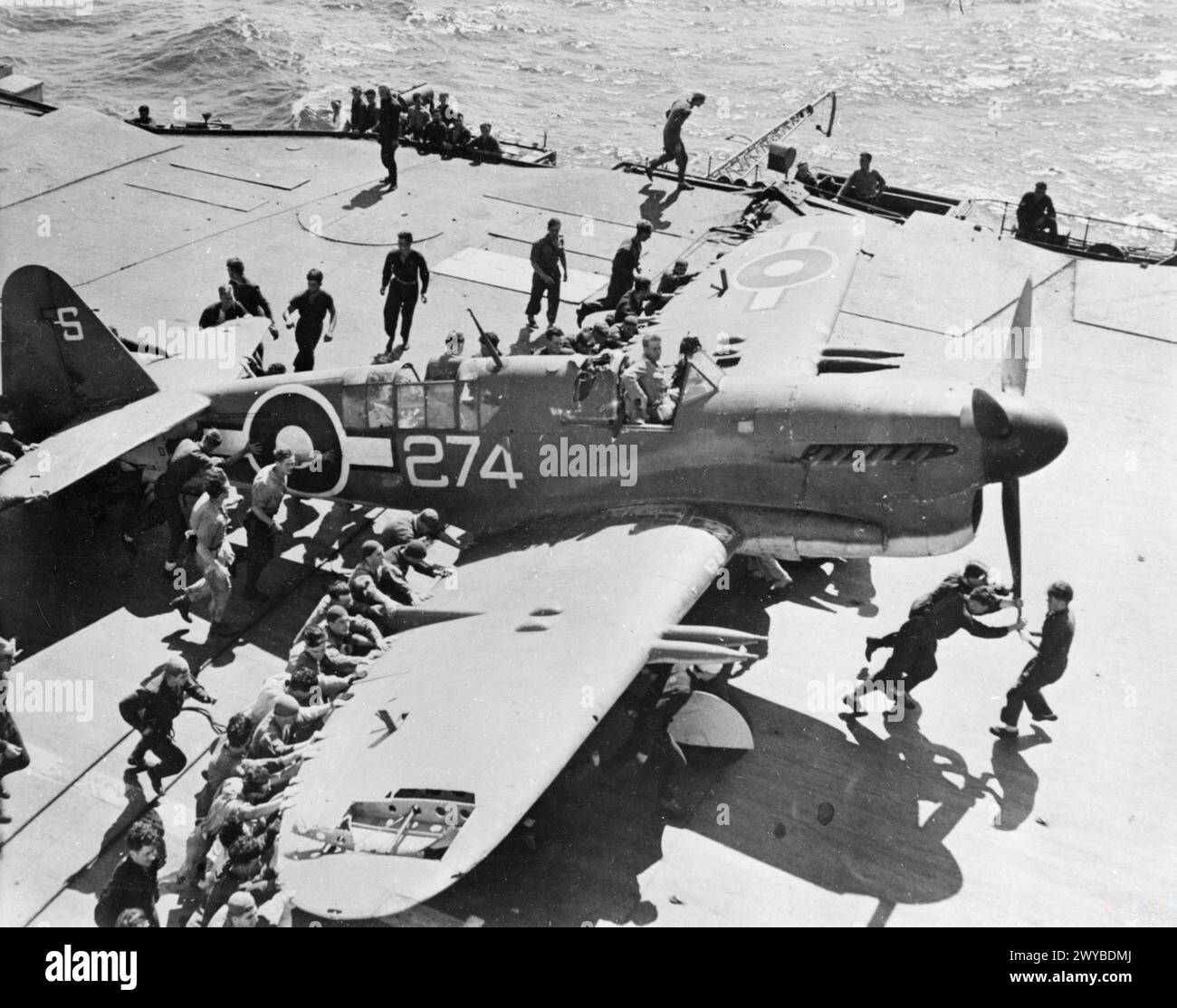 MIT HMS UNERMÜDLICH VOR DER JAPANISCHEN KÜSTE. JULI 1945, AN BORD DES SCHIFFES, DER MIT DER BRITISCHEN PAZIFIKFLOTTE KURZ VOR DER KAPITULATION DER JAPANER OPERIERTE. - Die Flugdeckparty schiebt einen beschädigten Firefly der 1772 Squadron entlang des Daches der UNERMÜDLICHEN, nachdem sie eine Notlandung gemacht hatte. Der Pilot war Sub Lieut (S) J Maclaren, RNVR. , Stockfoto