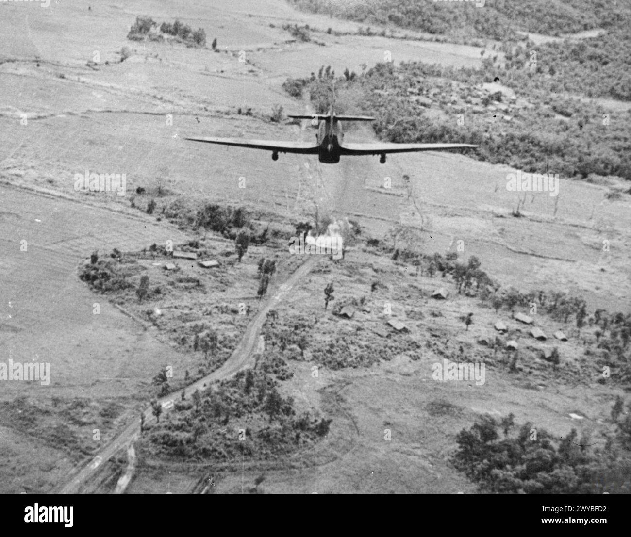 Ein Hawker Hurrikan Mark IIC der No. 42 Squadron RAF, gesteuert von Flying Officer Campbell, taucht ein, um eine Brücke in der Nähe einer Siedlung an der Tiddim Road in Manipur, Indien, anzugreifen, während Bomben von einem früheren Flugzeug auf das Ziel explodieren. Stockfoto