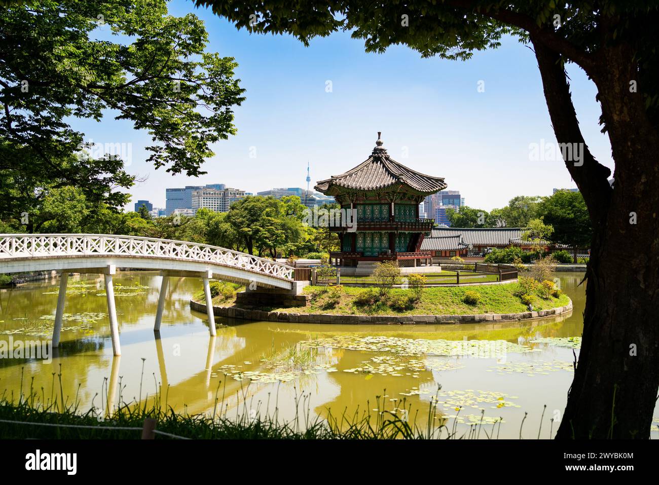 Südkorea, Seoul. Gyeongbokgung Palastbereich Garten und Park. Hyangwonjeong Pavillon und Brücke. Skyline der Stadt im Hintergrund. Sommerreisen. Stockfoto