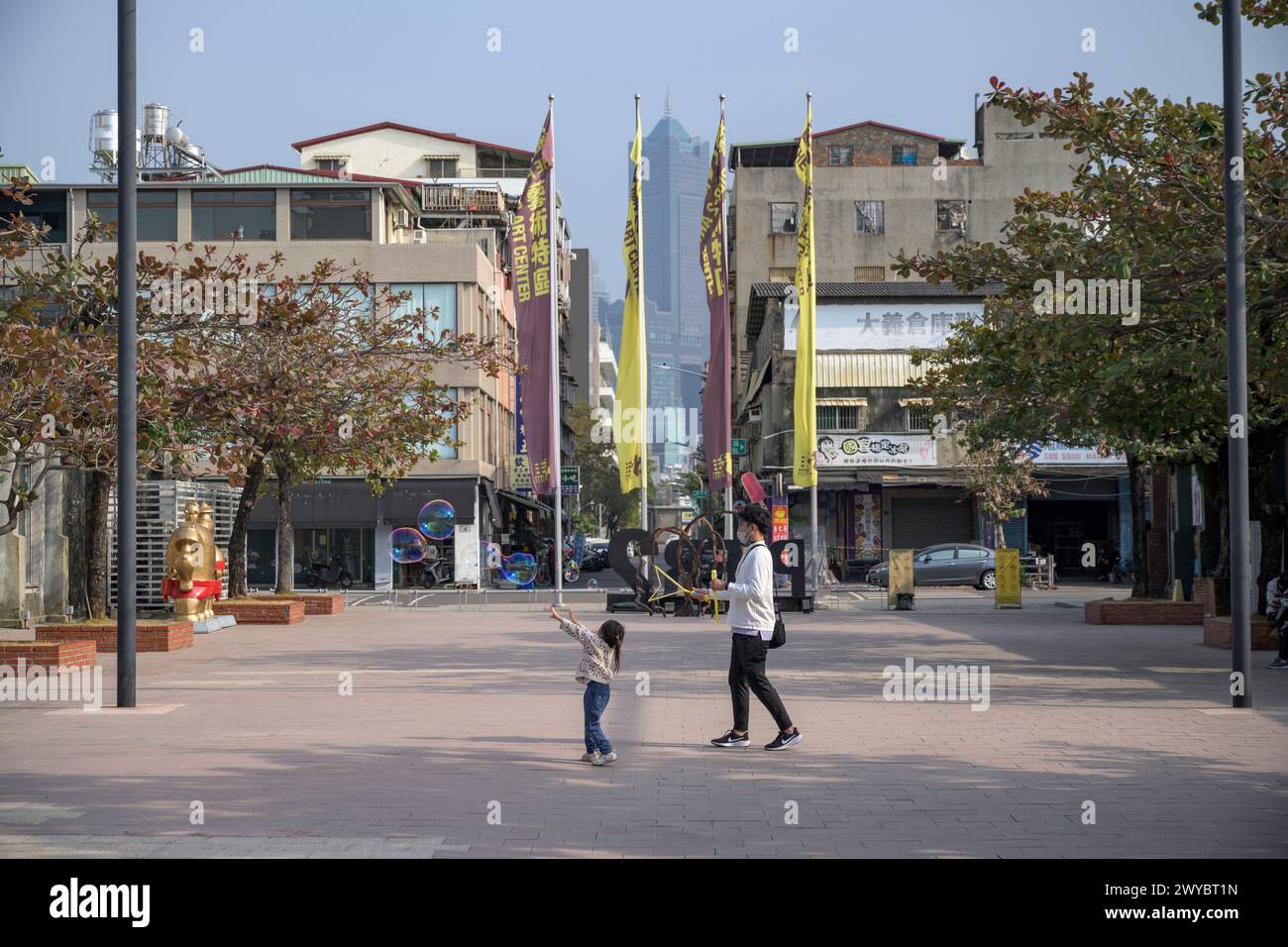 Ein Kind läuft Seifenblasen auf einem geräumigen Stadtplatz, der von Menschen und Stadtgebäuden umgeben ist Stockfoto
