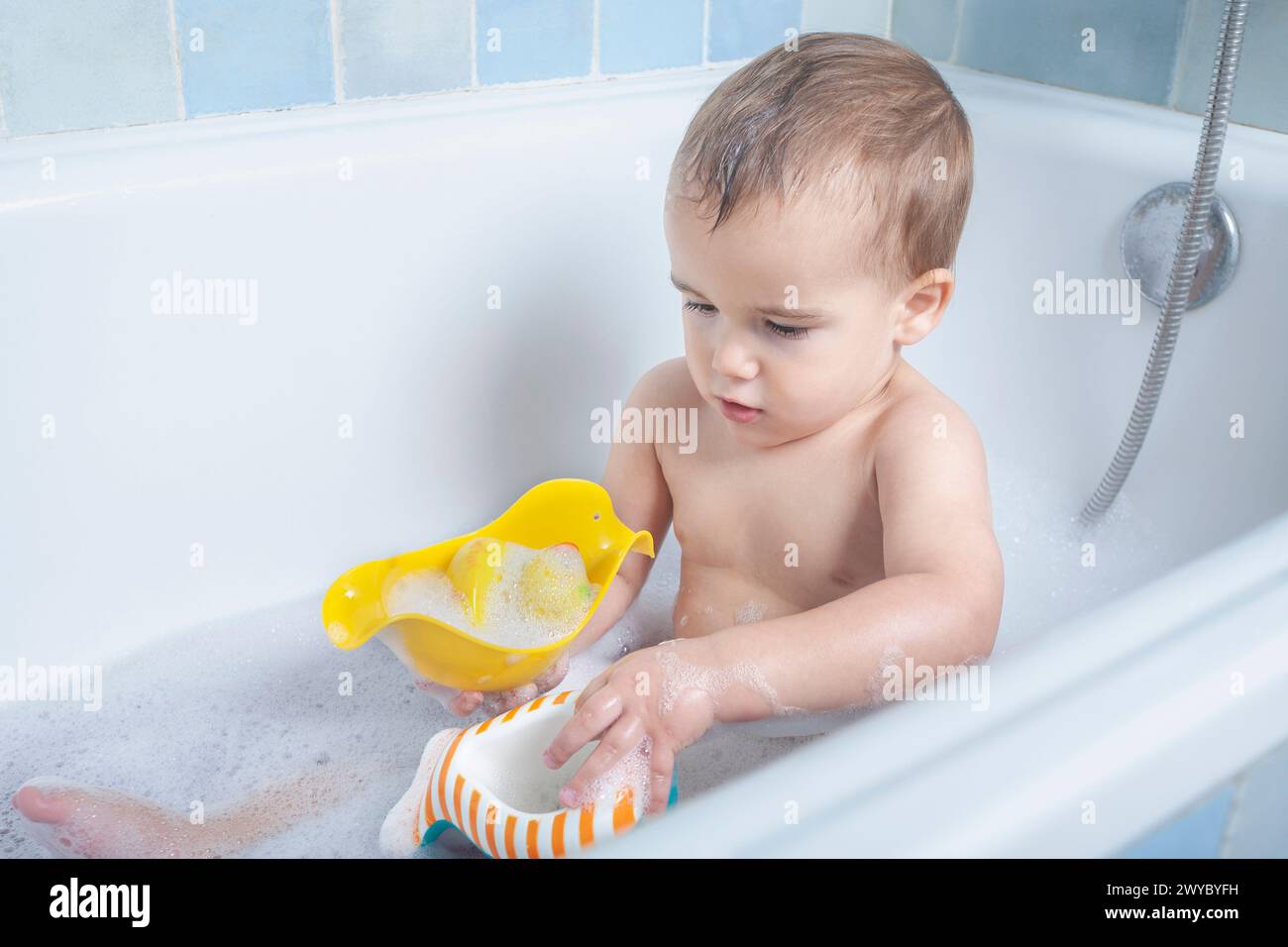 Das Kind kichert, während es mit dem Badewasser spielt, sodass es in der Badewanne spritzt und lächelt. Stockfoto