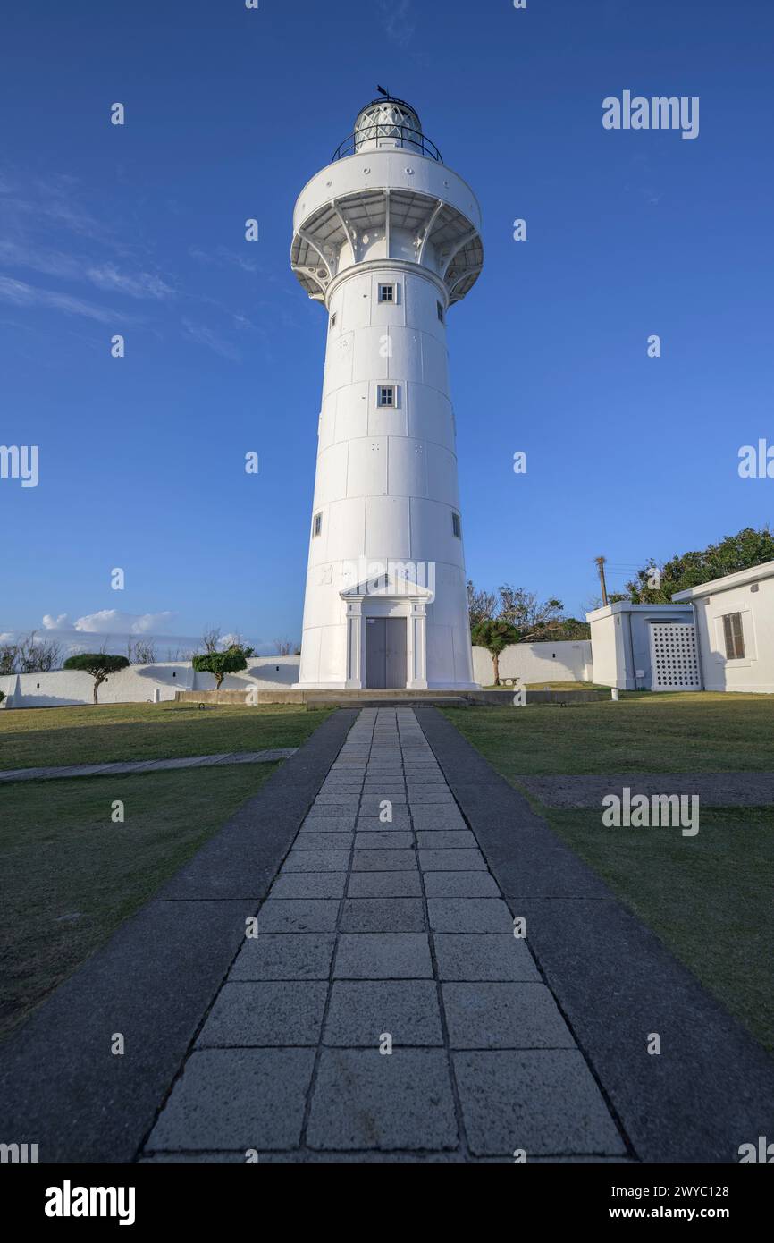 Ein majestätischer weißer Leuchtturm steht hoch unter einem klaren blauen Himmel mit einem Pfad, der zu ihm führt Stockfoto