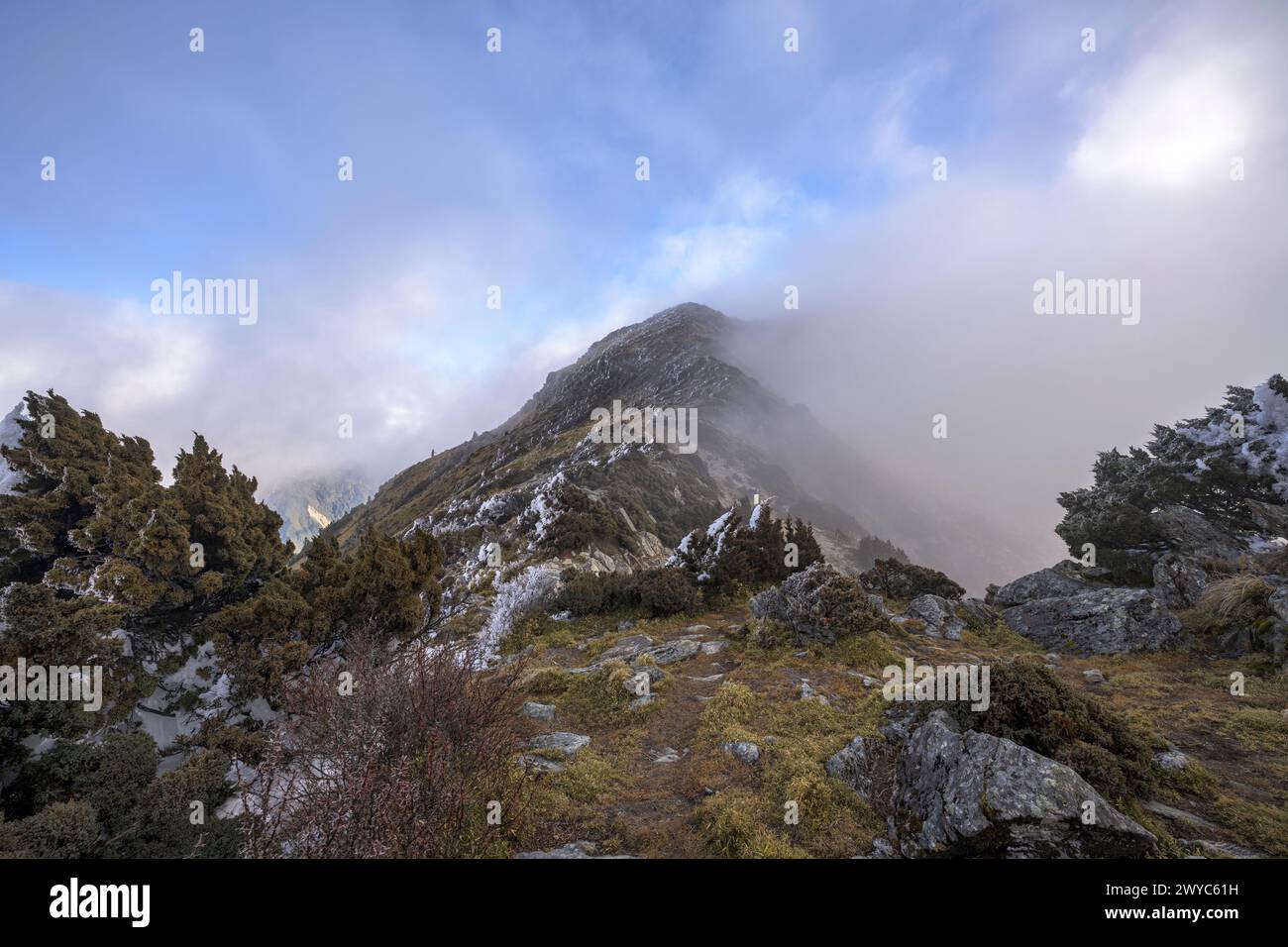 Der Gipfel eines Berges, der kaum durch sich ausbreitende Wolken sichtbar ist, schafft eine ätherische Landschaft voller Geheimnisse Stockfoto