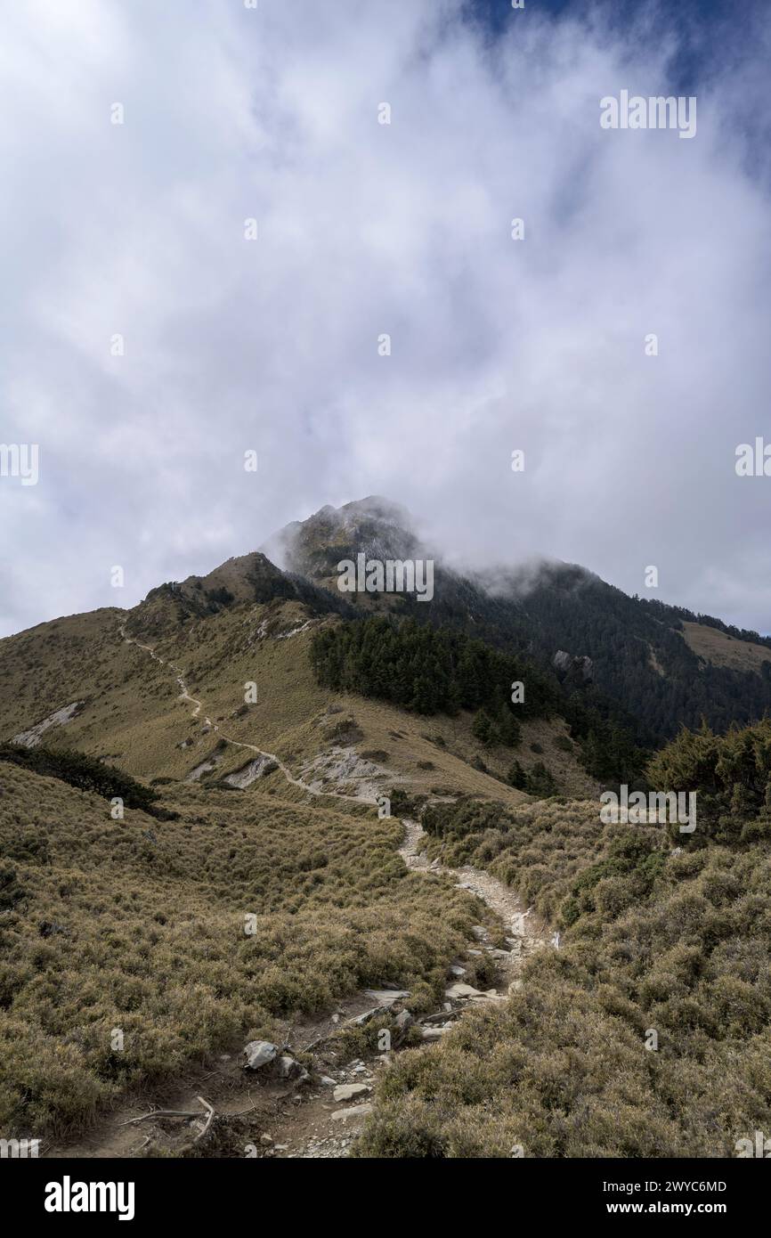 Der Gipfel eines Berges, der kaum durch sich ausbreitende Wolken sichtbar ist, schafft eine ätherische Landschaft voller Geheimnisse Stockfoto