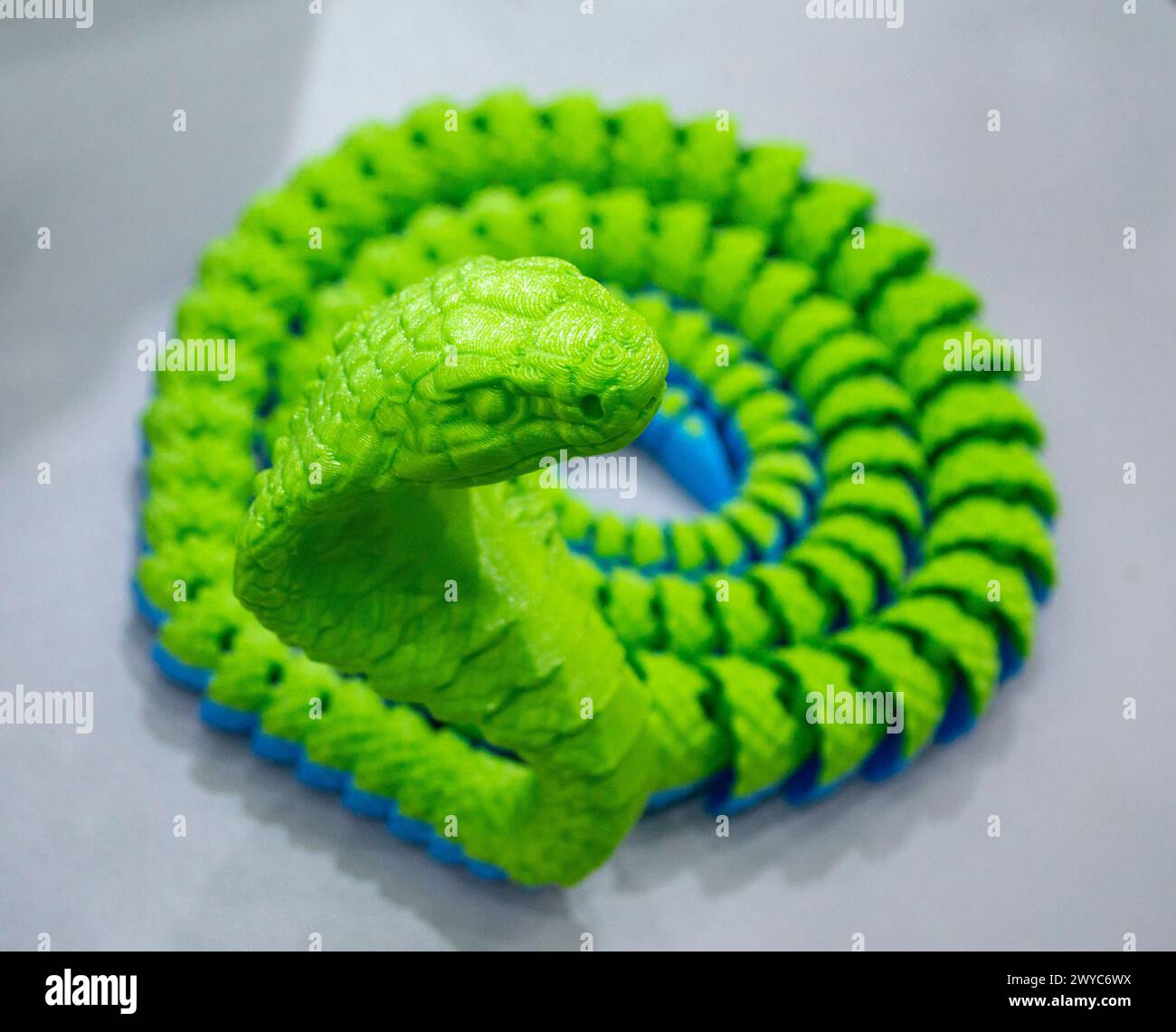 Grünes Schlangenspielzeugmodell, gedruckt auf einem 3D-Drucker aus geschmolzenem Kunststoff. Vom 3D-Drucker erzeugtes Objekt in Schlangenform. Detaillierter grüner Prototyp auf 3D-Drucker in Nahaufnahme gedruckt. Neue moderne Additivtechnologien Stockfoto