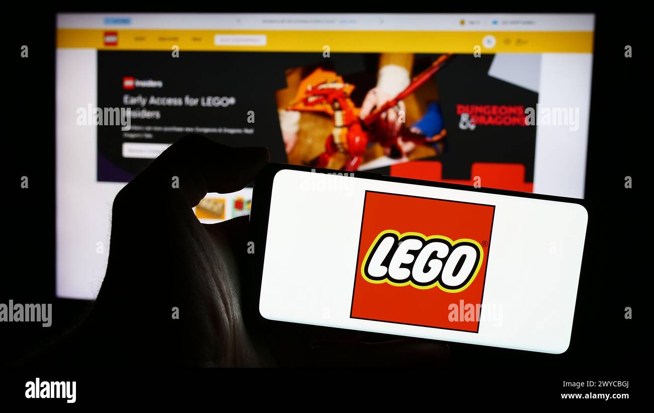 Person, die ein Mobiltelefon mit dem Logo des dänischen Bauspielzeugherstellers LEGO hält, WIE vor der Webseite. Schwerpunkt auf dem Display des Telefons. Stockfoto