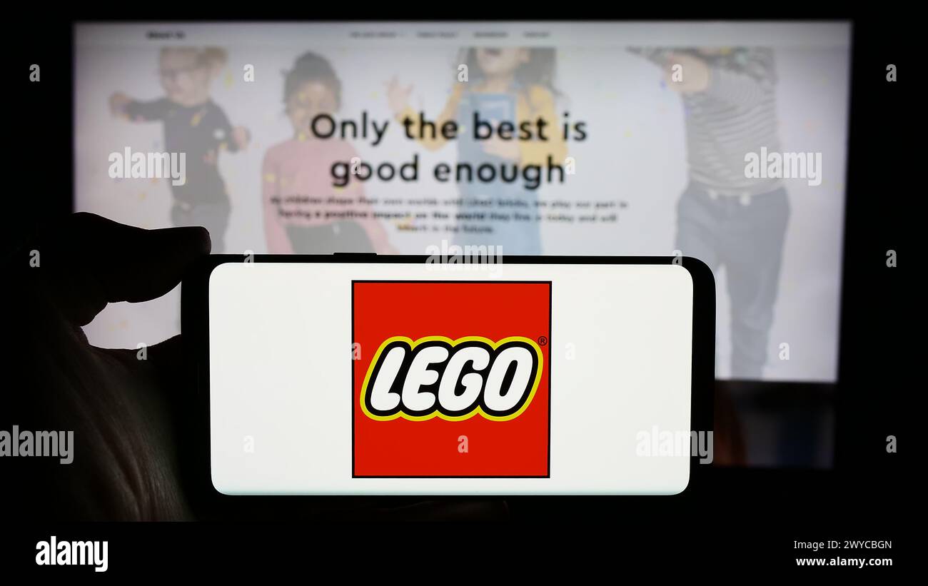 Person, die ein Handy mit dem Logo des dänischen Bauspielzeugherstellers LEGO hält, WIE vor der Website des Unternehmens. Schwerpunkt auf dem Display des Telefons. Stockfoto