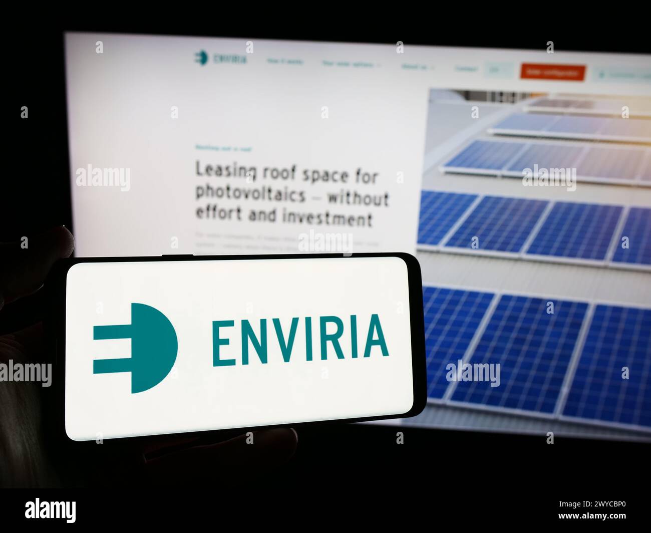 Person mit Smartphone und Logo des deutschen Solarunternehmens ENVIRIA Energy Holding GmbH vor der Website. Schwerpunkt auf dem Display des Telefons. Stockfoto