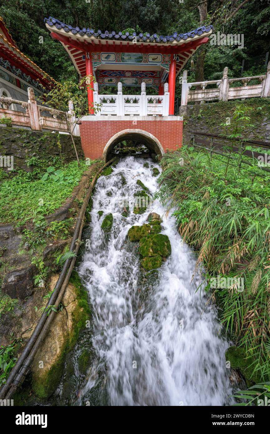 Eine malerische Struktur im Pagodenstil steht über einem schnell fließenden Bach in einer üppigen Umgebung und ist ein Beispiel für traditionelle asiatische Architektur Stockfoto