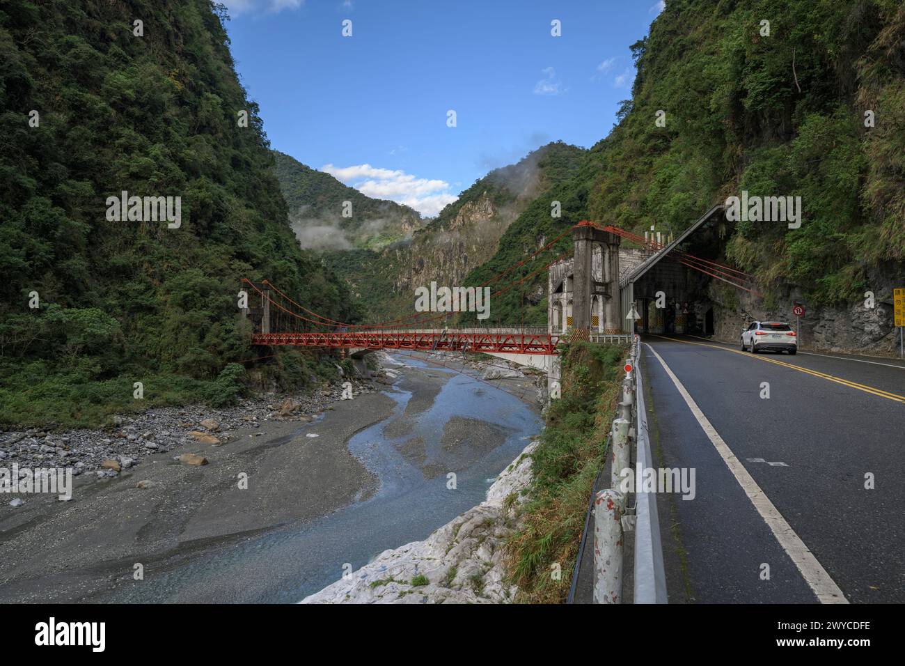 Ruhige Berglandschaft mit einer roten Hängebrücke und einem fließenden Fluss Stockfoto