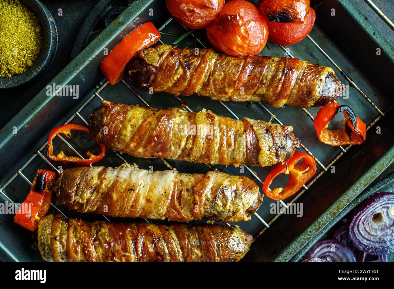 Gegrillter Speck mit Würstchen mit Tomaten und Zwiebeln auf dem Blech von oben, Nahaufnahme Stockfoto