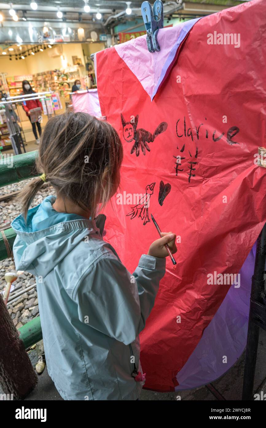 Mädchen malt sorgfältig Kalligraphie auf eine große Himmelslaterne, um sich das chinesische Neujahr zu wünschen Stockfoto
