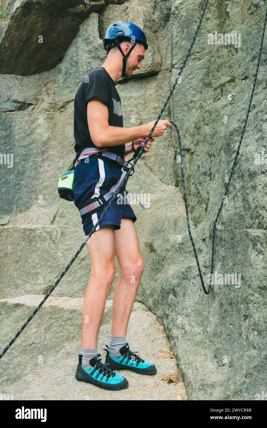 Junger Mann in Ausrüstung, der draußen vor Steinfelsen steht und sich bereit macht, zu klettern. Trainingsbereich für Outdoor-Aktivitäten. Extremsport. Stockfoto