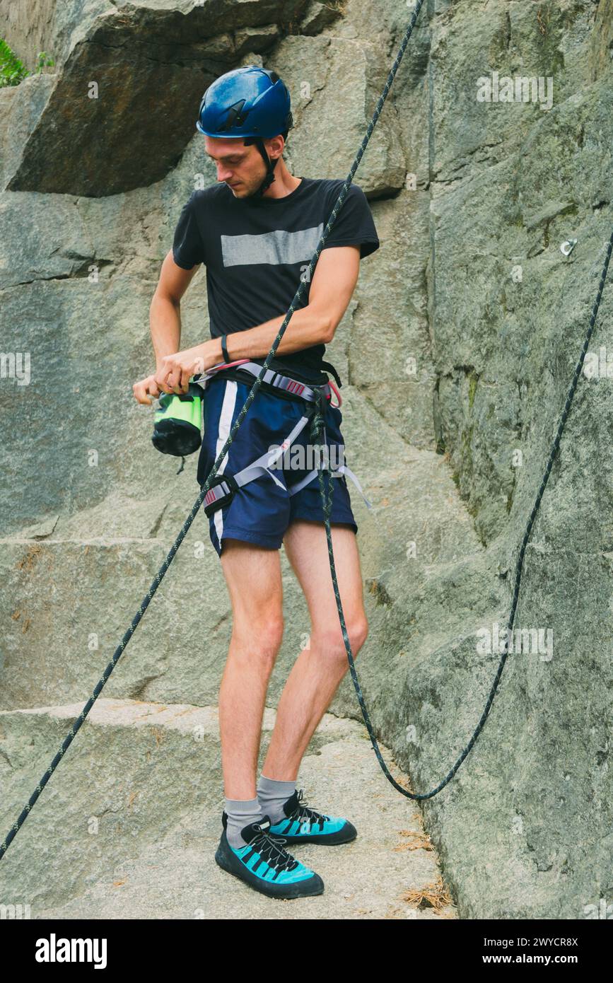 Junger Mann in Ausrüstung, der draußen vor Steinfelsen steht und sich bereit macht, zu klettern. Trainingsbereich für Outdoor-Aktivitäten. Extremsport. Stockfoto