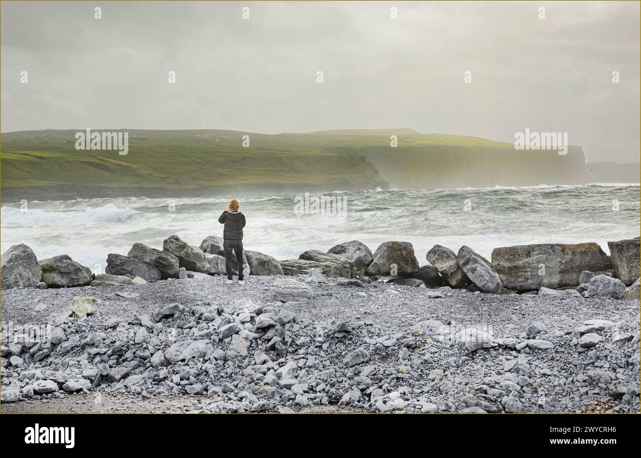 Eine Frau stand an einem Stoney Strand mit Blick auf das Meer an einigen Klippen, während ein Sturm tobt Stockfoto