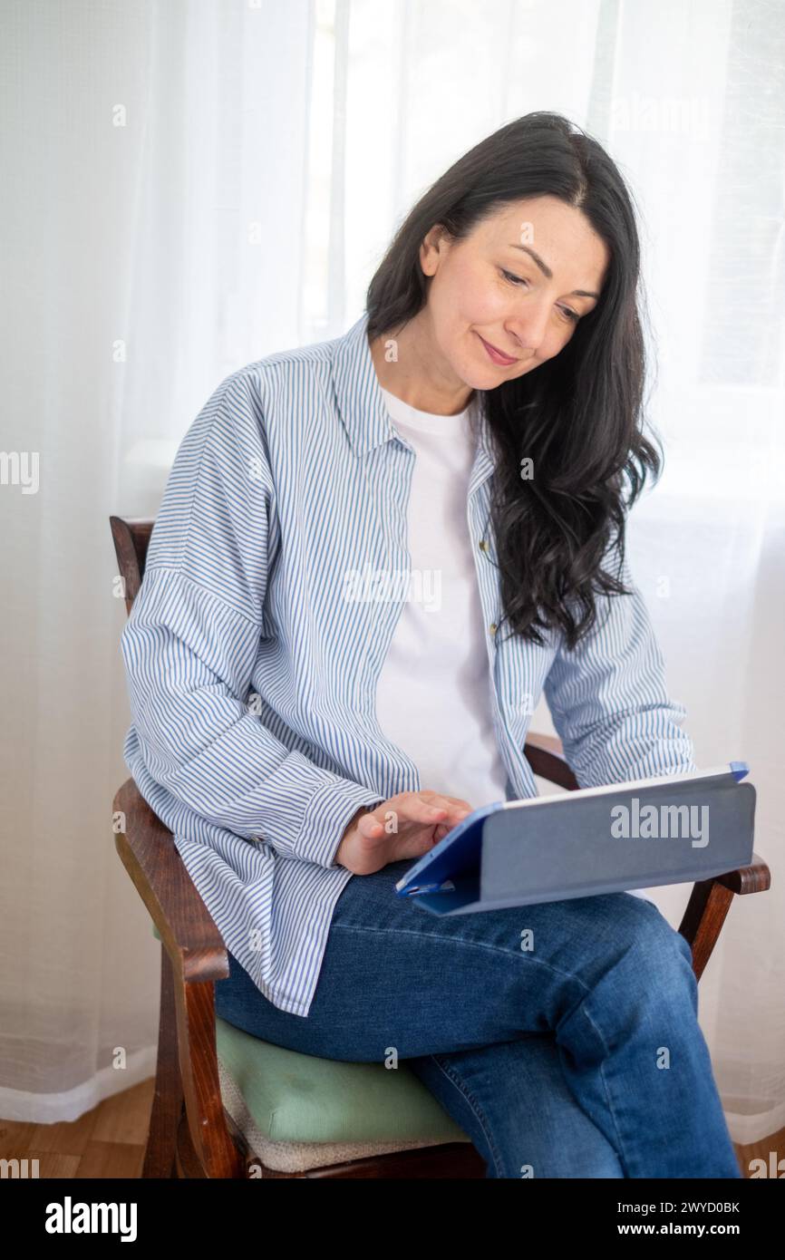 Glückliche Frau mittleren Alters, die ein Tablet verwendet, spiegelt die Interaktion mit digitalen Medien in ihren Reifen Jahren wider, eine Mischung aus Komfort und Technologie und lebenslanger Lehren Stockfoto